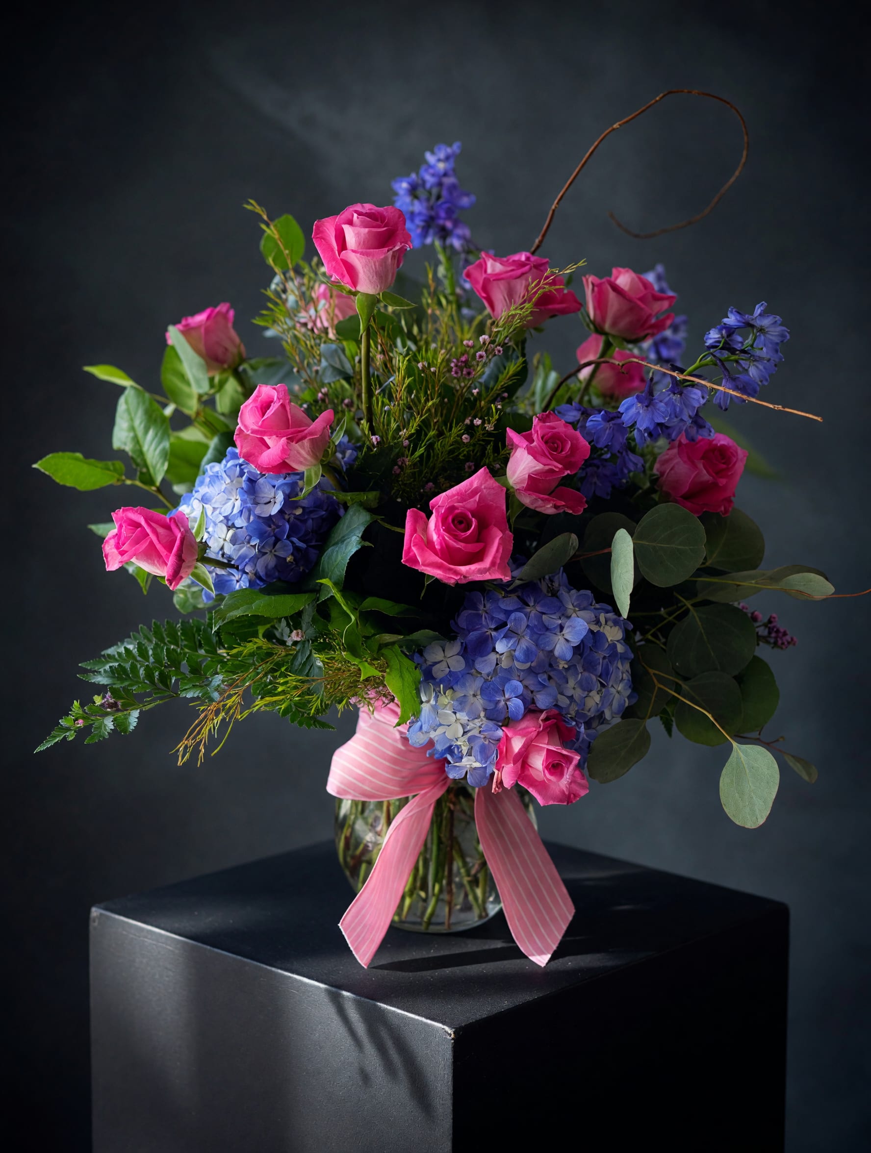 Pink roses and blue hydrangeas in a glass vase with a pink ribbon