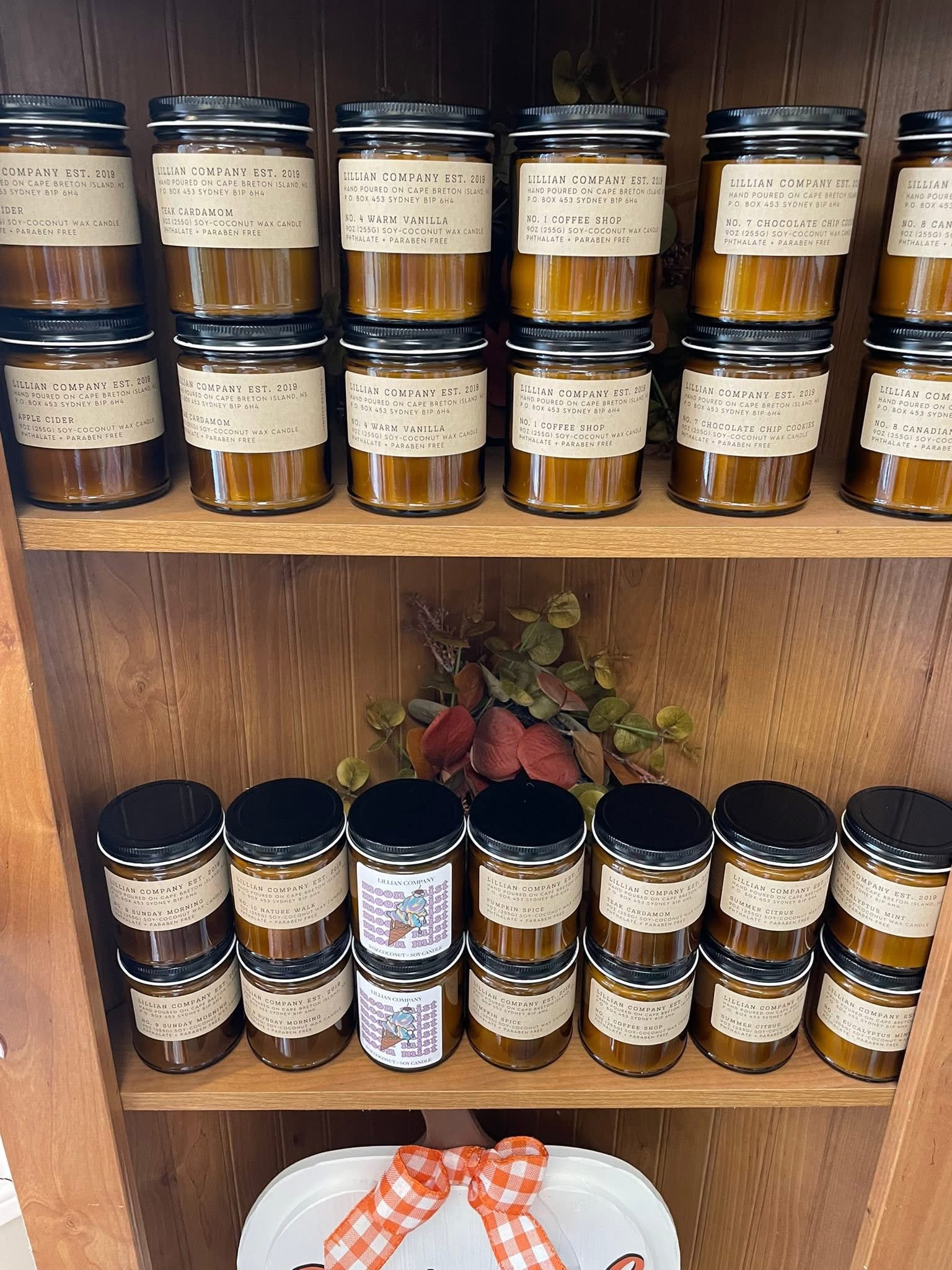 Shelves of labeled jar candles with a plaid ribbon on a gift basket below