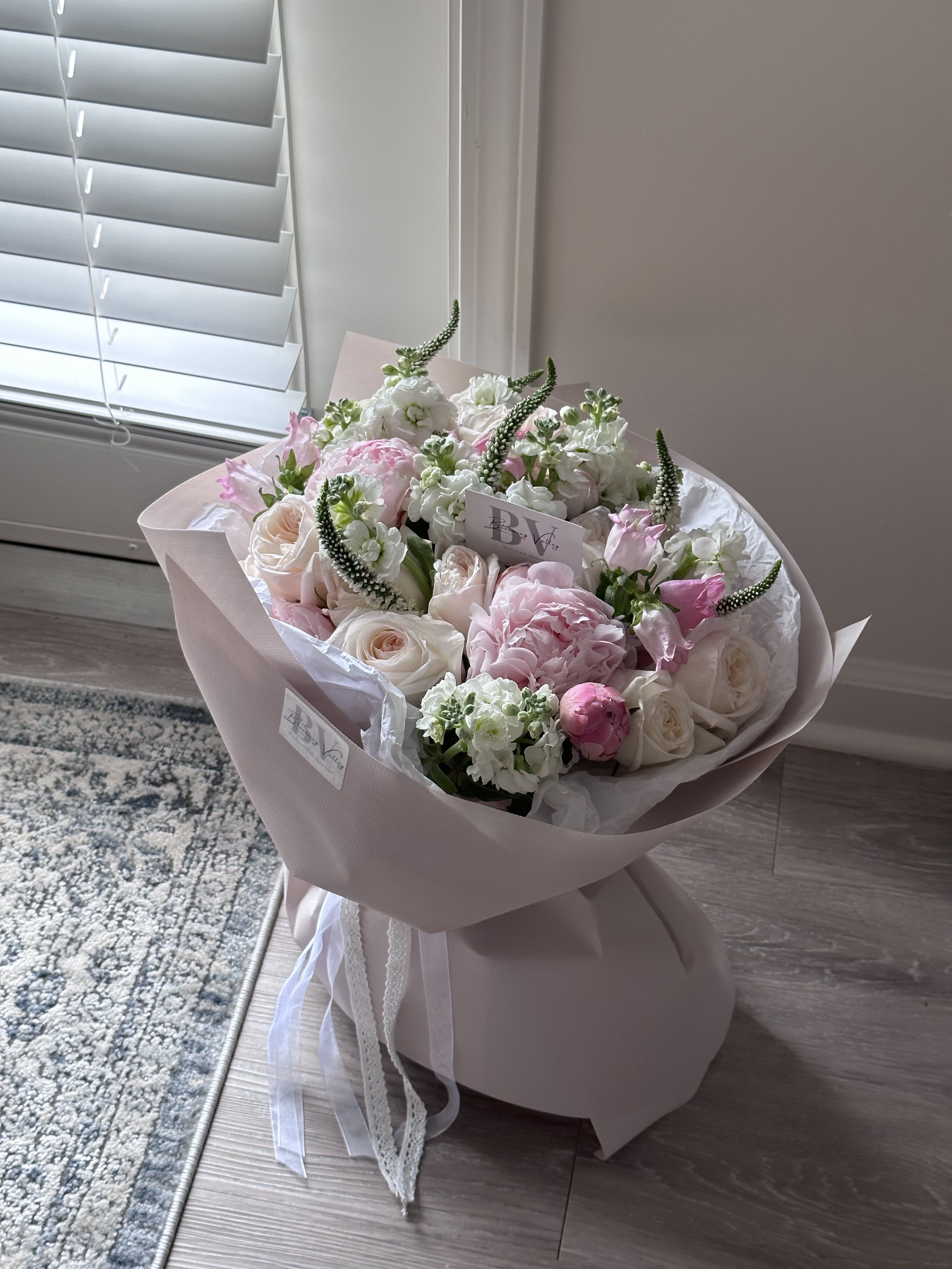 Blush Harmony - A delicate symphony of soft pinks, creamy whites, and fresh greens, Blush Harmony captures the essence of romance and elegance. Featuring peonies, garden roses, stock, and veronica, this bouquet is wrapped in tender blush tones with flowing ribbons, evoking a sense of refined charm. Perfect for celebrating love, beauty, or simply brightening someone’s day with a touch of floral grace.