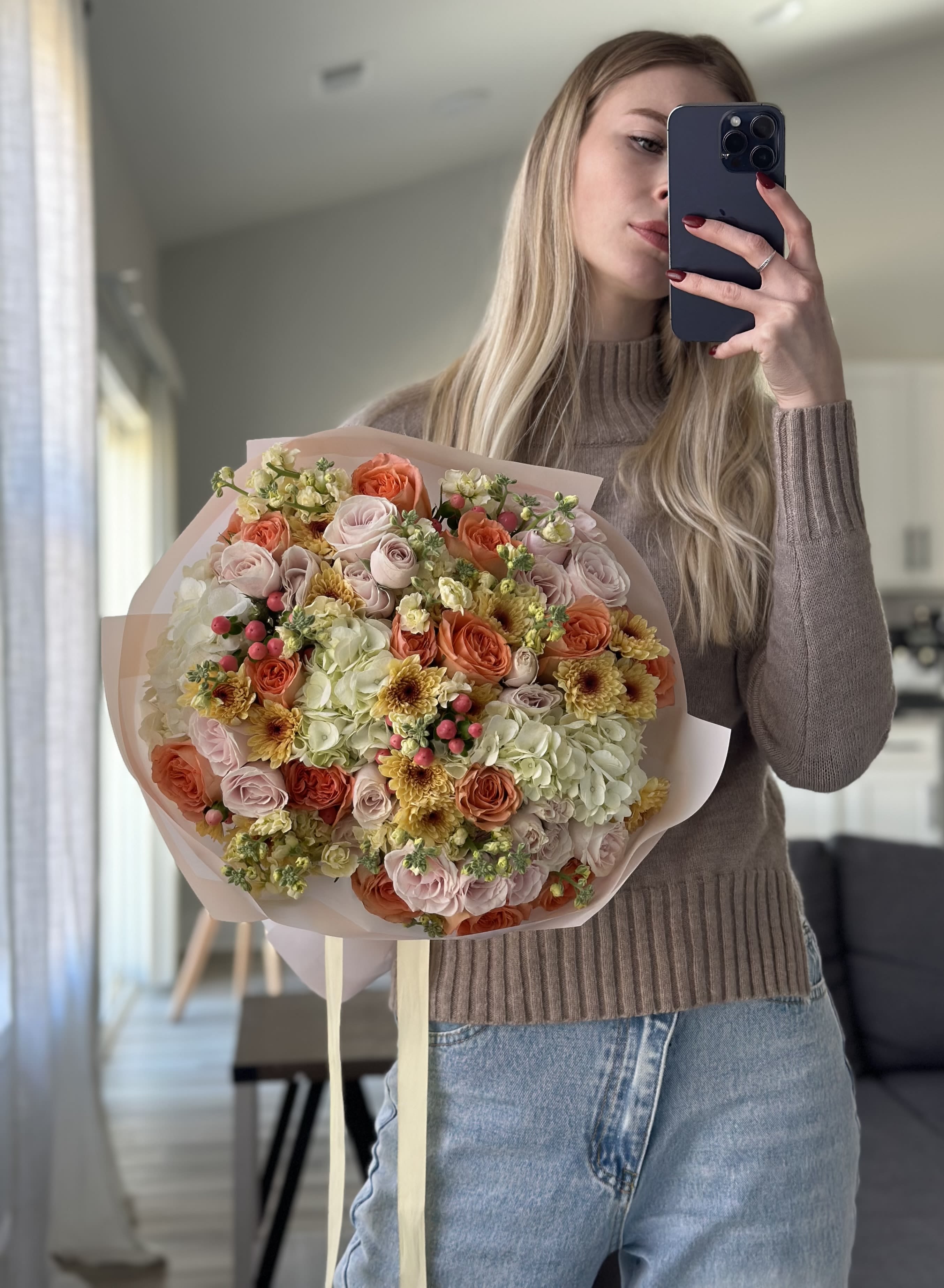 Large bouquet of peach, pink, and cream flowers wrapped in pale paper