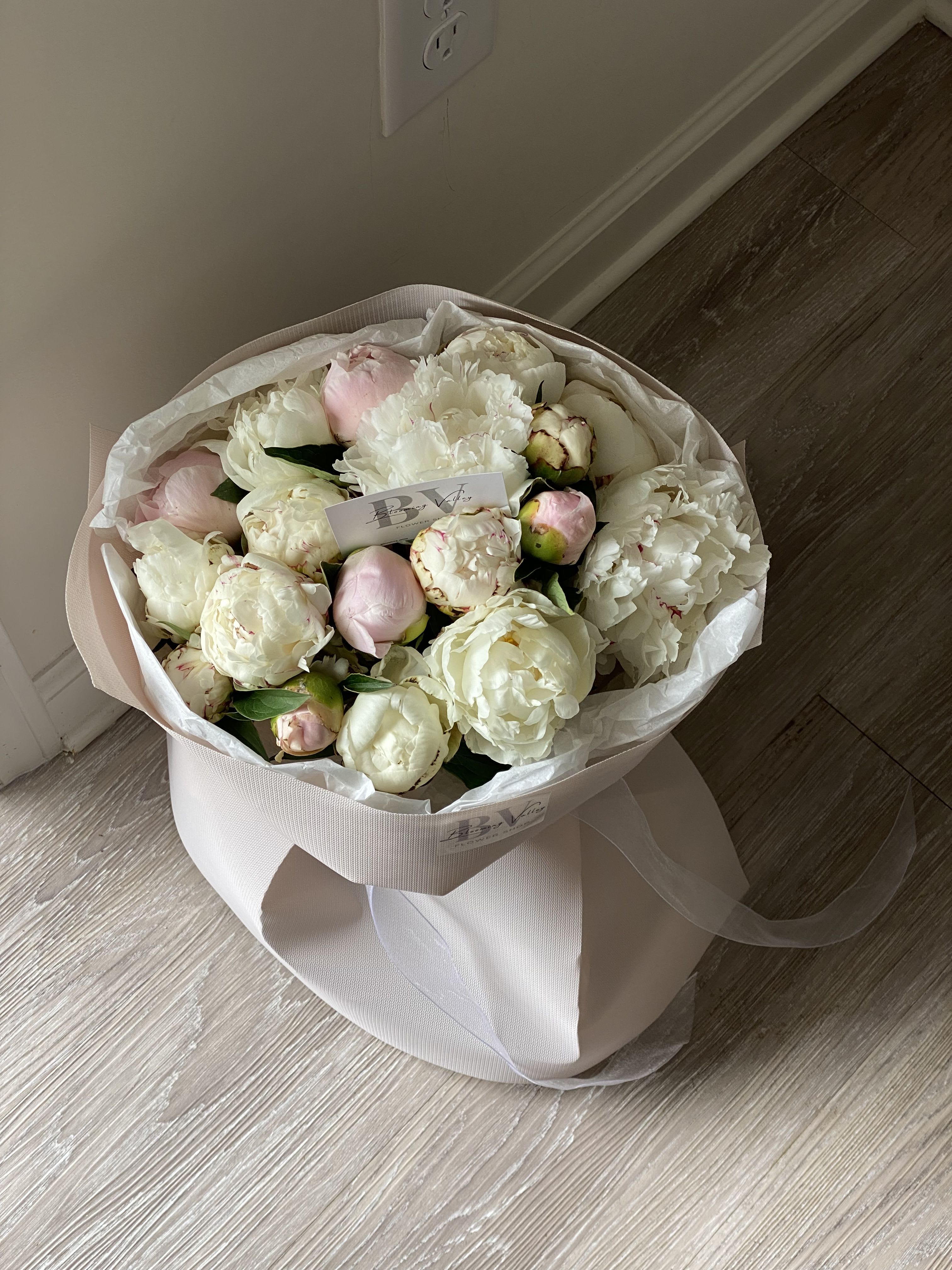 Bouquet of white and pale pink peonies wrapped in blush paper
