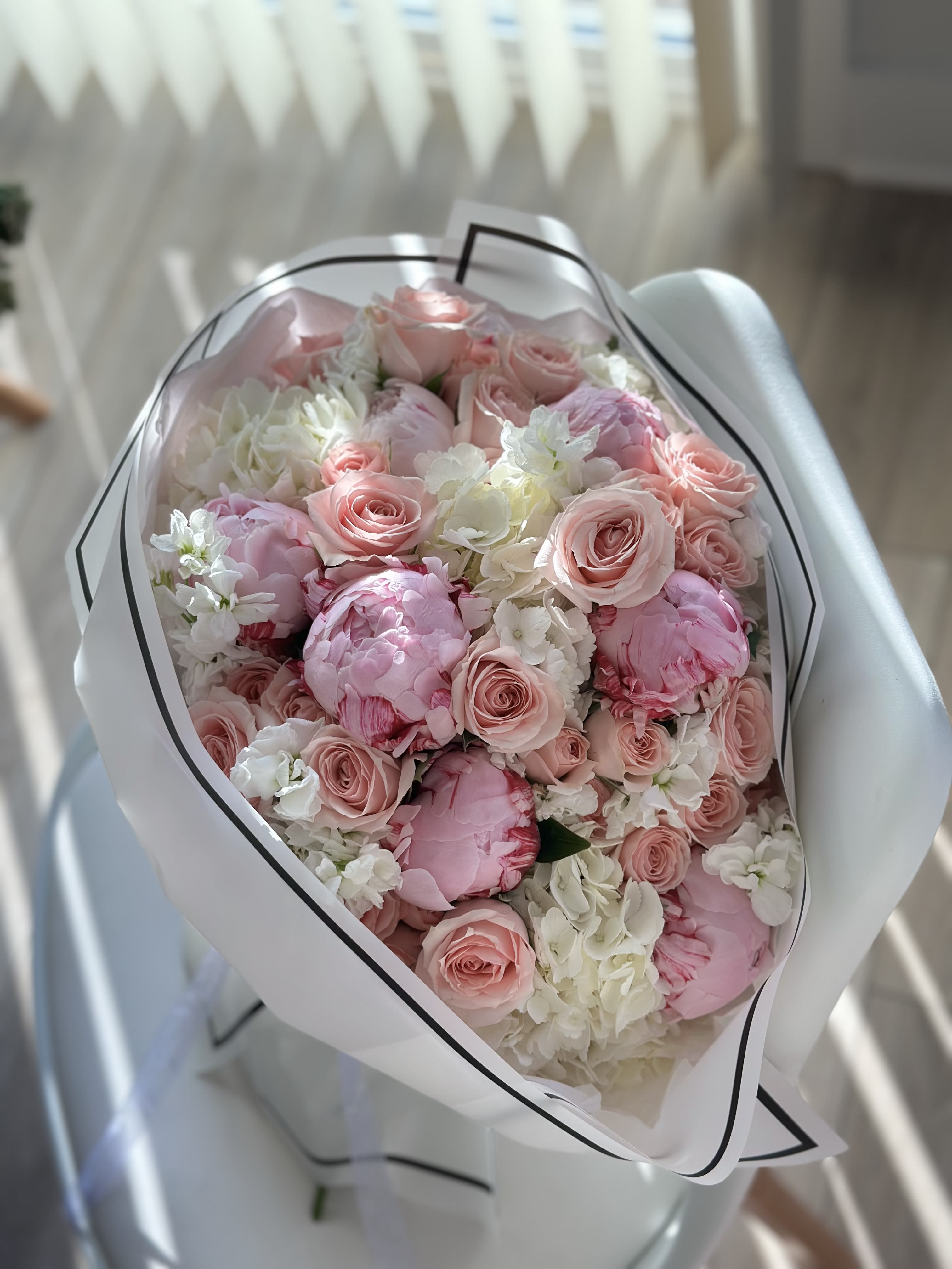 Morning Grace - A luminous arrangement of blush roses, full pink peonies, and creamy hydrangeas, wrapped in elegant white with a black trim. Morning Grace captures the freshness of a new day and the softness of a whispered “I love you.” Perfect for birthdays, weddings, or simply to brighten someone’s world.