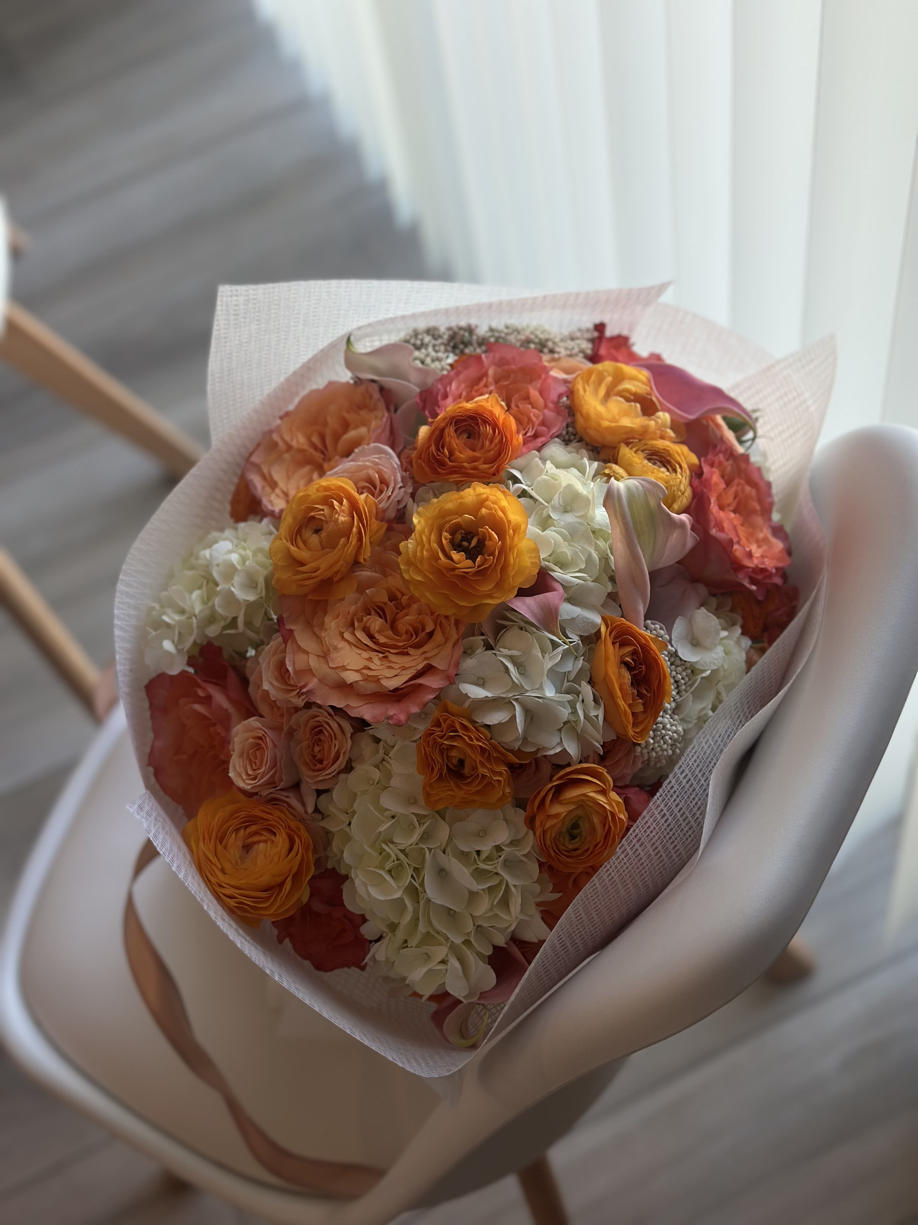 Bouquet of orange and peach flowers with white hydrangeas in pink wrap
