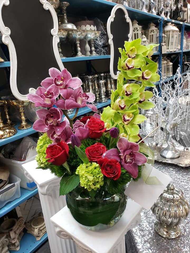 Arrangement of pink and green orchids with red roses in a glass vase
