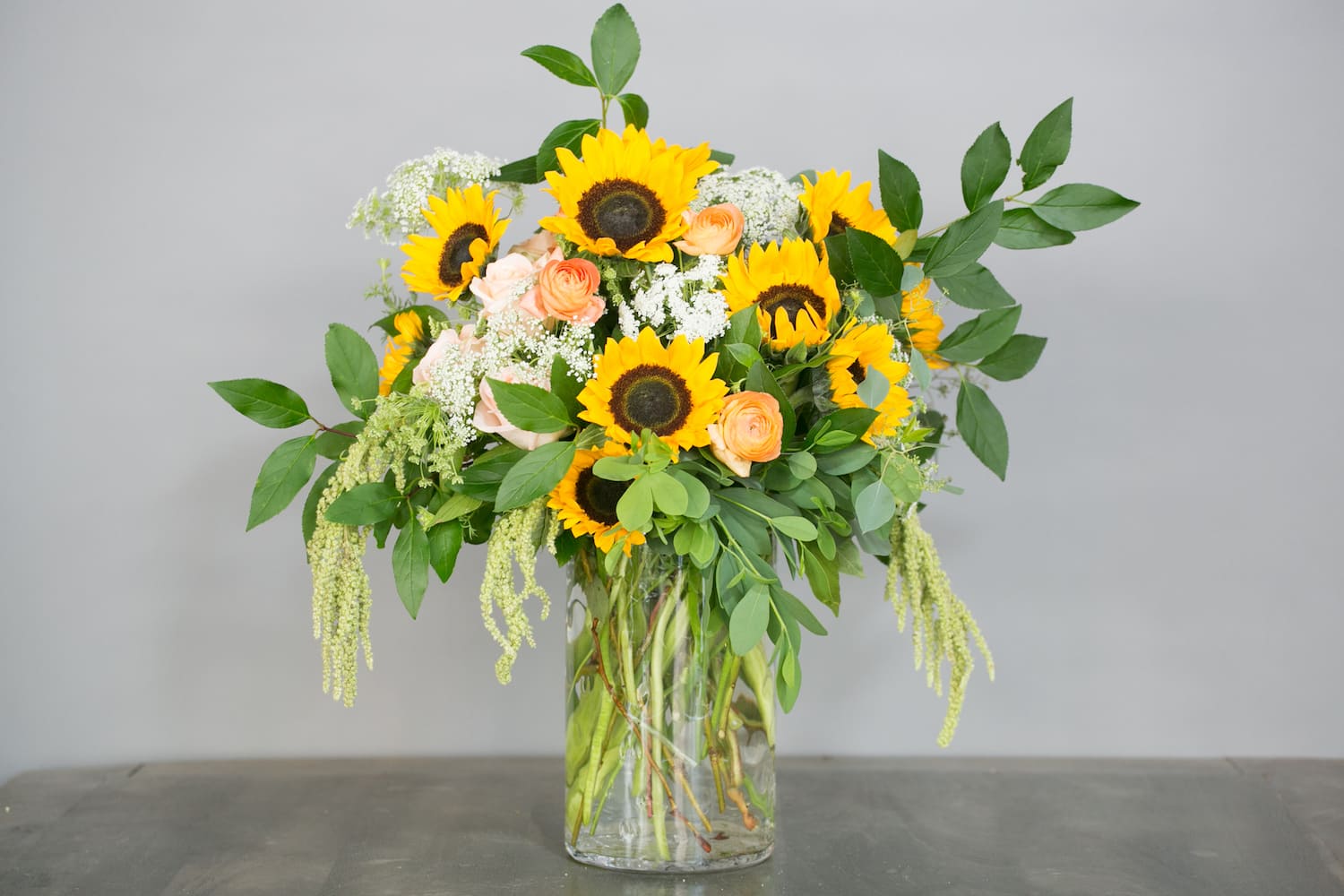 Sunflower and peach rose arrangement in a clear glass vase