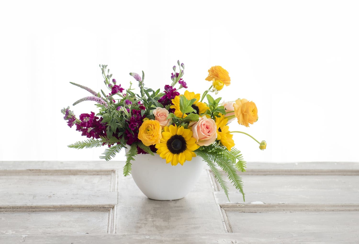 Mixed bouquet in a white vase with sunflowers, roses, and orange blooms