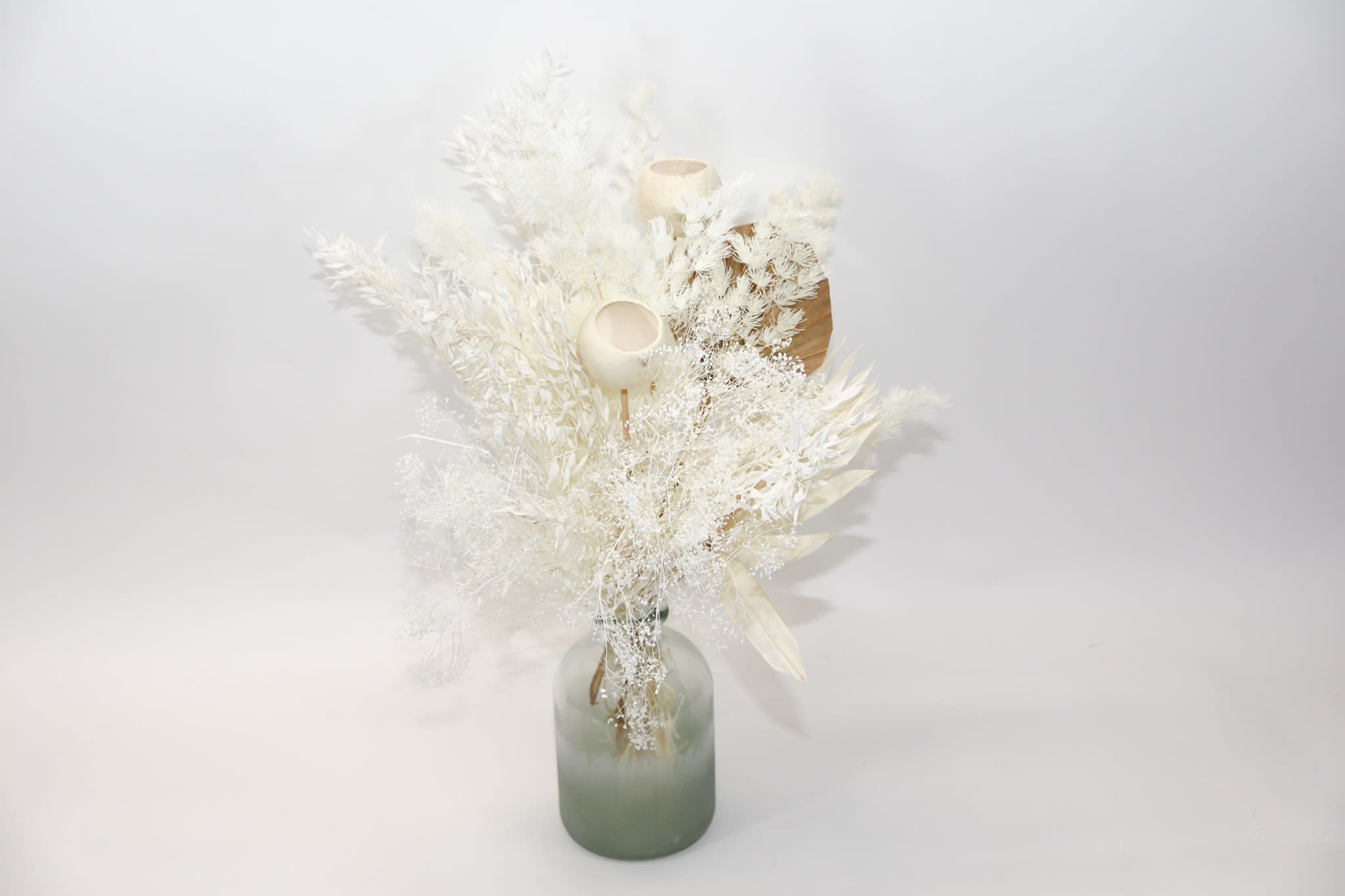 White dried floral arrangement in a frosted glass vase