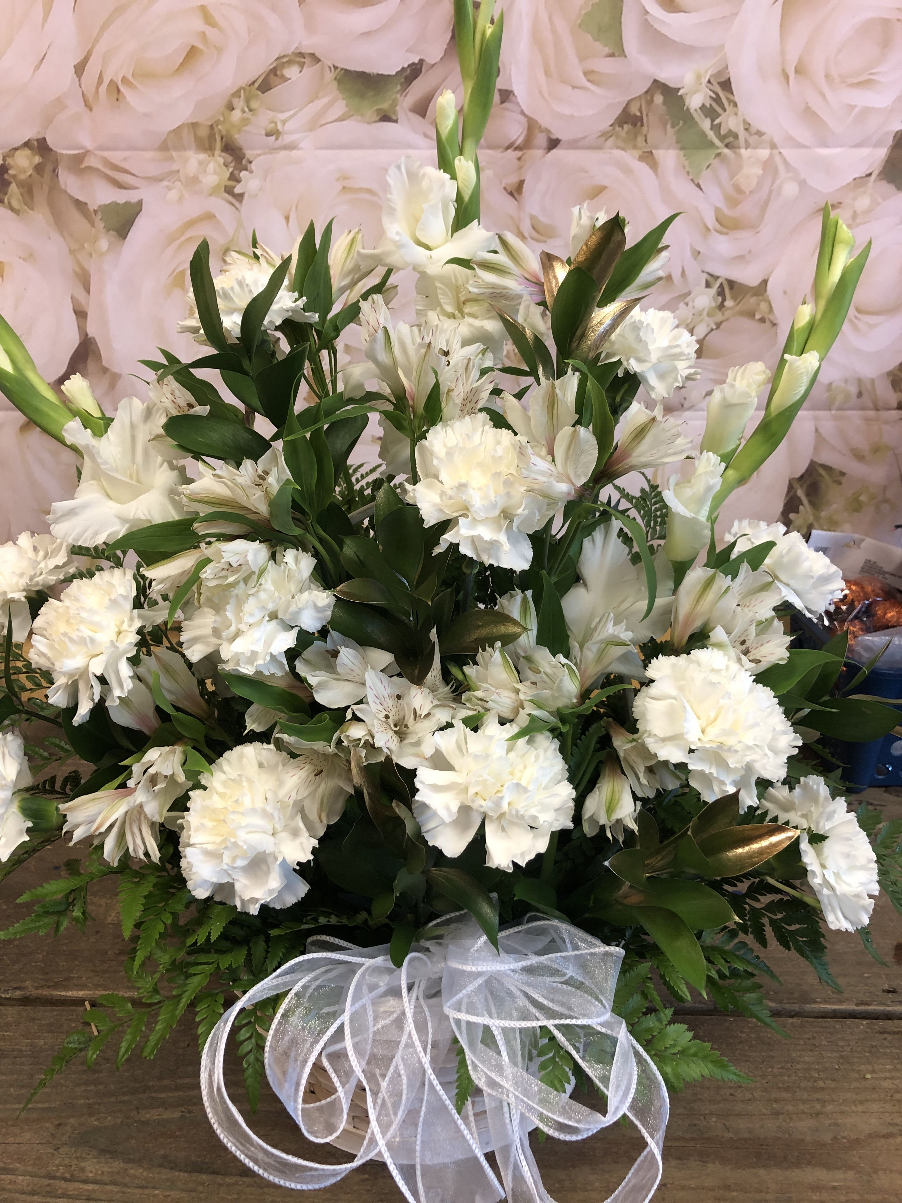 White floral arrangement in a basket with a sheer ribbon bow