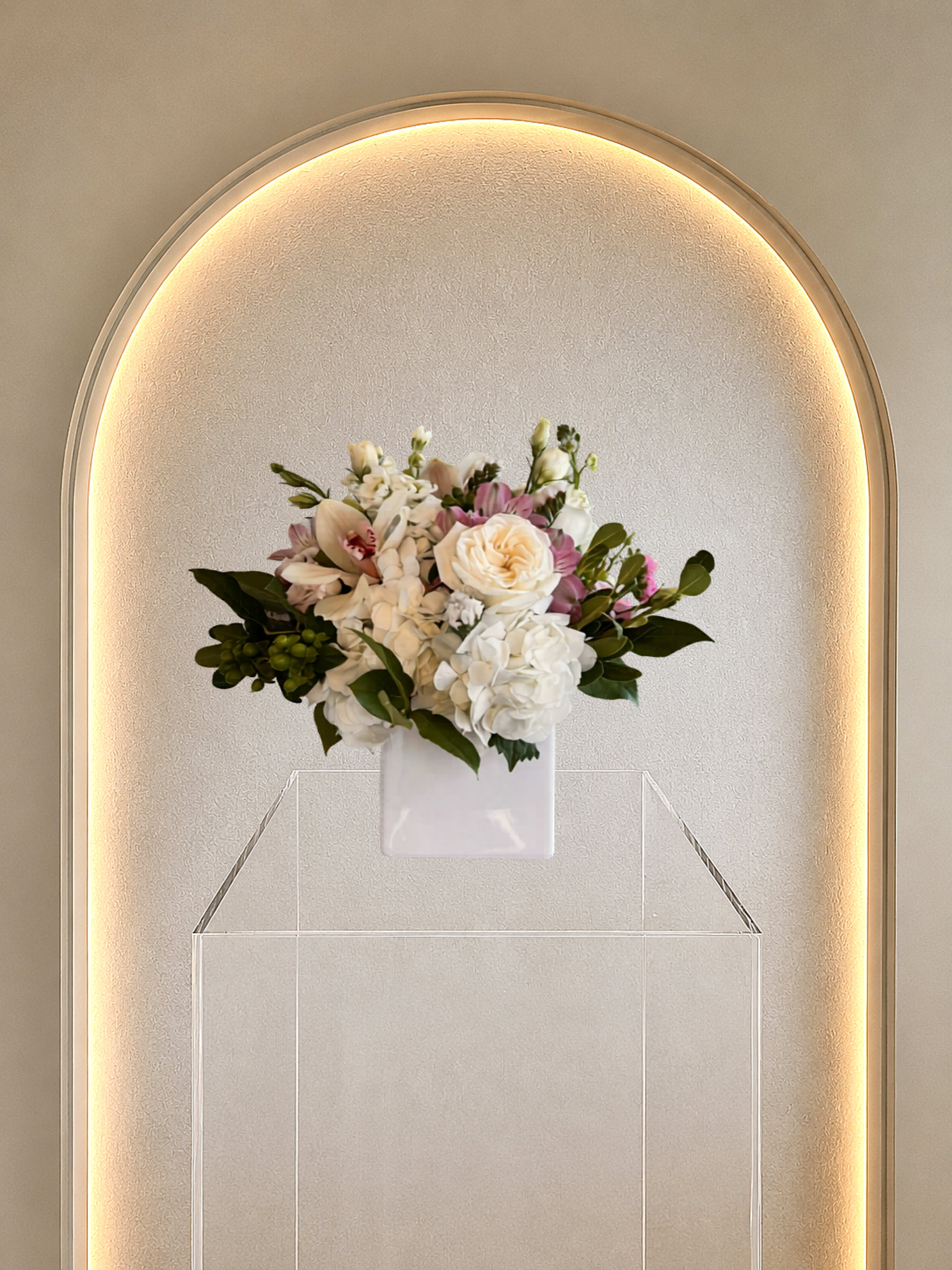 Cymbidium Daydream - Classic compact rounded mix of cymbidium, hydrangea, rose and lisianthus in a white square ceramic vase. 