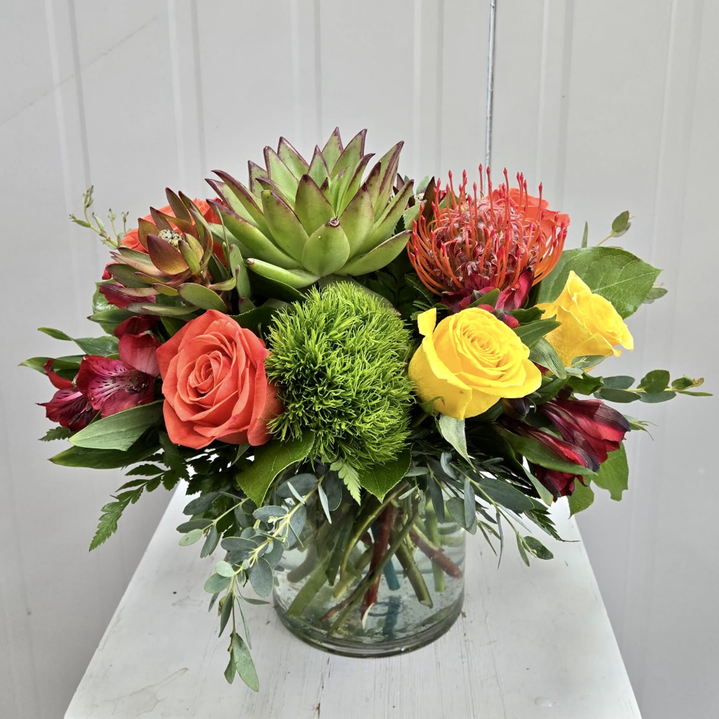 Summer Sunset - This Arrangement includes a Succulent, Pin Cushion, Green Trix, Red Alstroemeria, Yellow Roses, Orange Roses and Safari Sunsets in a Clear Glass Vase. Or as Similar as Possible. 