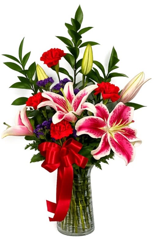 Lovely Lilies - These amazing lilies are sure to delight!  Beautiful pink lilies, red carnations, filler flowers and foliage hand arranged in a clear cylinder vase.  Approximately 25" tall and 18" wide.
