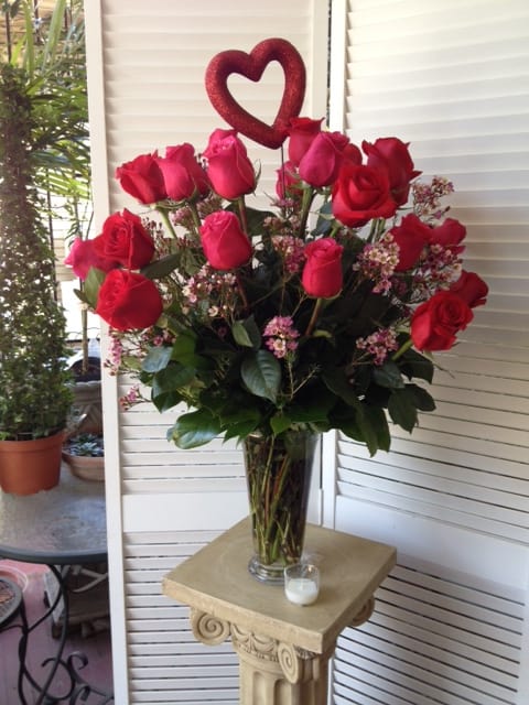Red roses in a clear glass vase with a heart topper