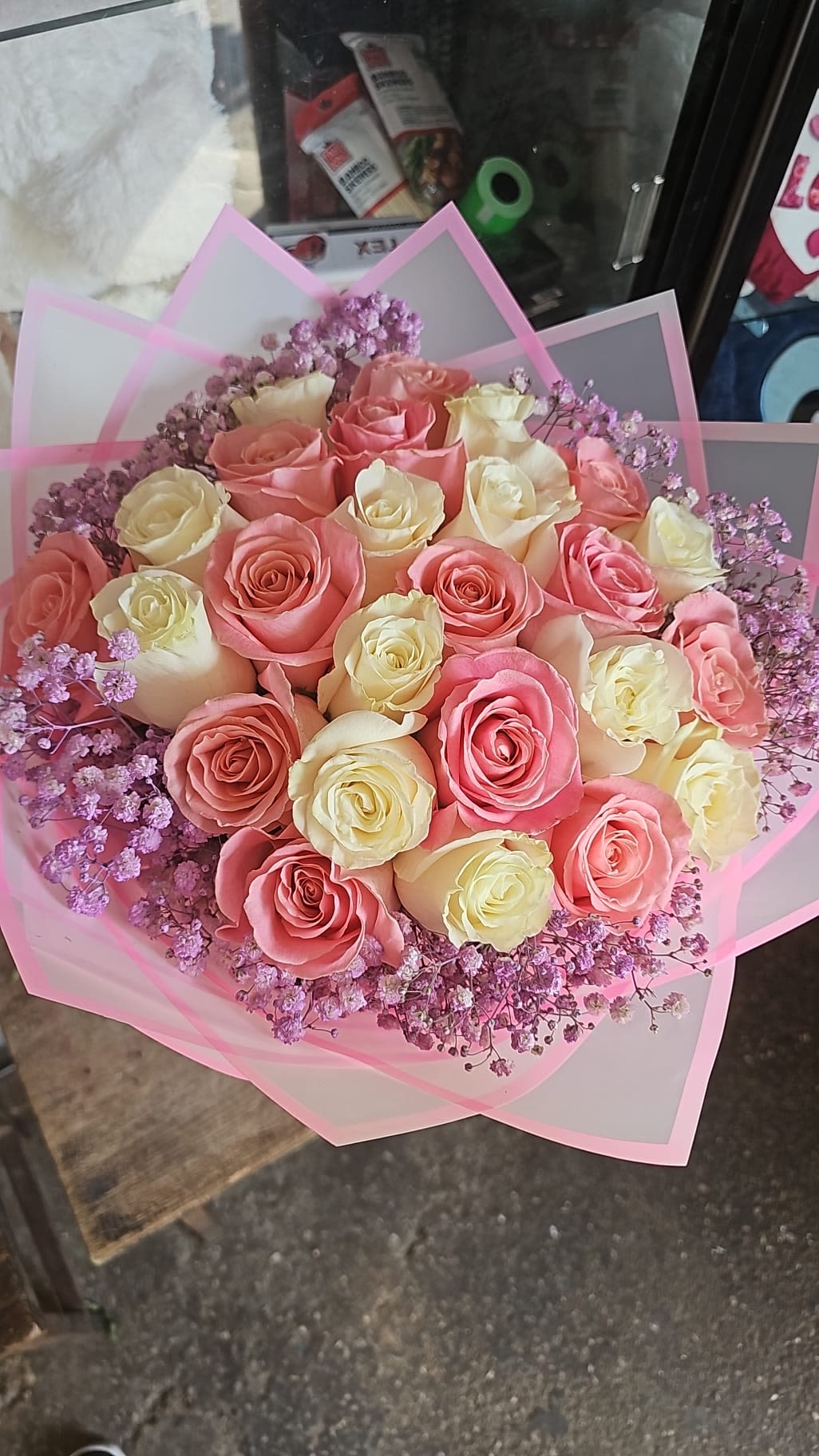 Round bouquet of pink and cream roses with lavender filler flowers wrapped in pink translucent paper
