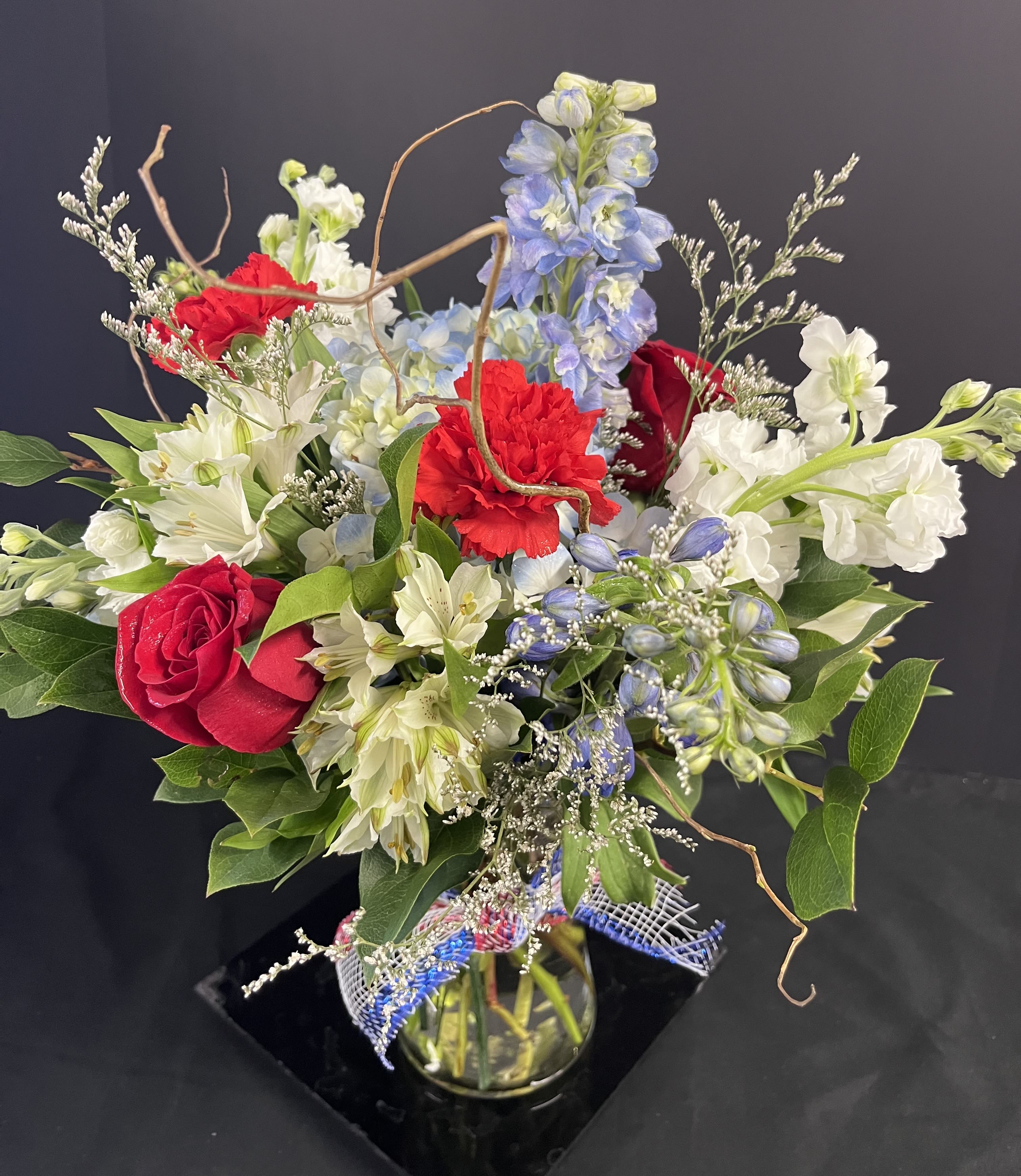 Mixed bouquet of red roses, white lilies, and blue flowers in a glass vase