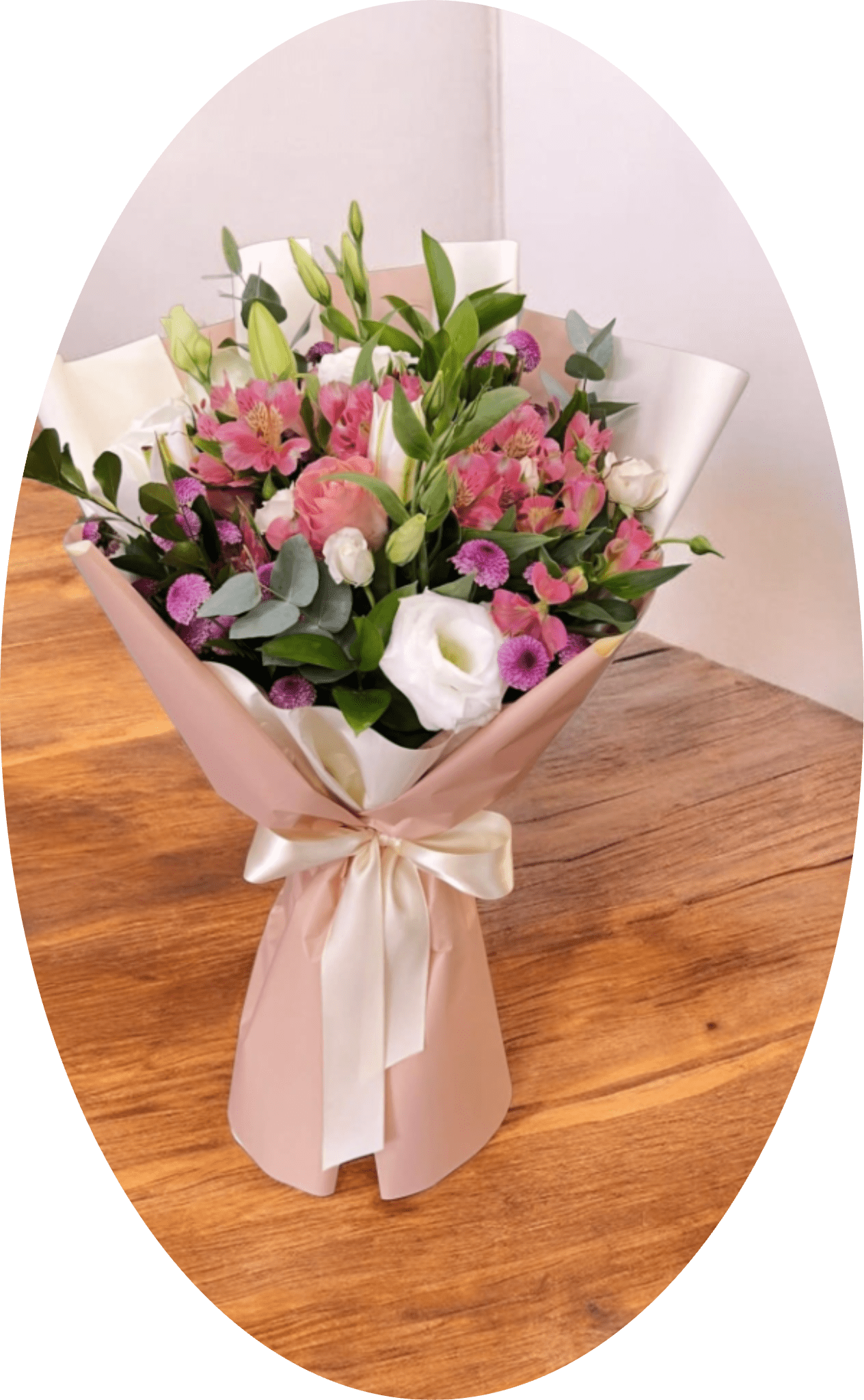 Sussane - A soft bouquet of pink alstroemeria, white lilies and lisianthus that reads like a gentle celebration - perfect as a birthday bouquet, anniversary flowers, Mother's Day gift, or a thoughtful just-because arrangement. The layered pastels of pink, white and touches of purple create a romantic, uplifting impression so the person you're sending it to will feel cherished and seen the moment the ribbon is untied.  This hand-tied arrangement pairs delicate alstroemeria and roses with dianthus and small purple filler blooms, plus glossy green foliage for fresh contrast. A few lily buds add graceful height and the lisianthus brings a soft, ruffled texture. Wrapped in blush pink paper with white inner wrap and finished with satin ribbon (wide white ribbon and pink wrapping paper accents), it arrives polished and ready to display.  Ideal for celebrating moms, partners, close friends, or anyone who appreciates soft, romantic florals-this bouquet suits small gatherings or intimate surprises. Arrange stems in fresh water on arrival and recut if needed to extend vase life; its compact hand-tied style makes it easy to place in most standard vases.