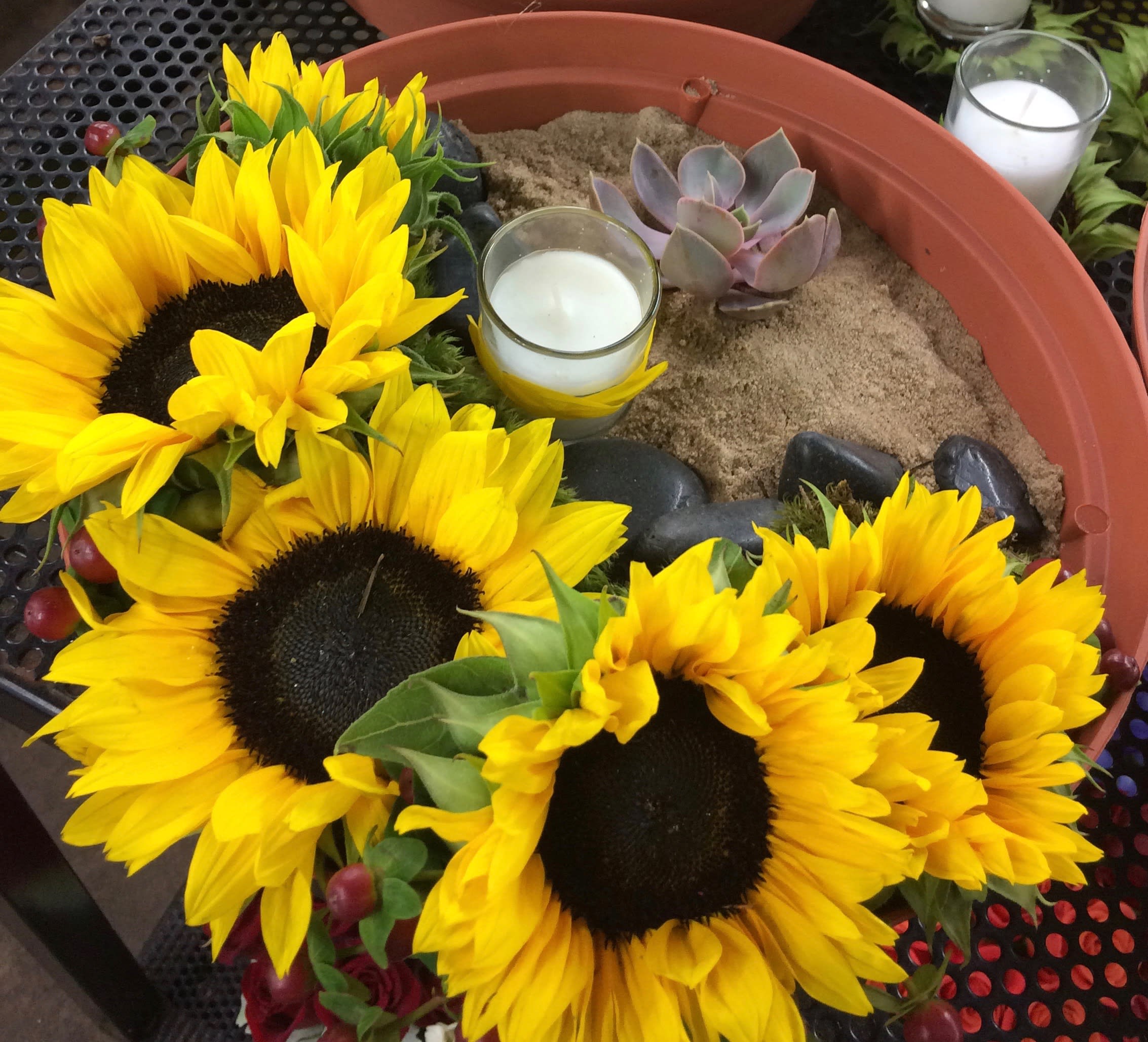 Sunflowers arranged around candles and a small succulent in a shallow planter