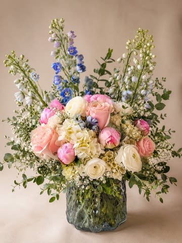 Iceberg Blooms - A fresh, airy arrangement inspired by the beauty of ice and soft garden blooms. Designed in a unique iceberg-style glass vase, this piece features blush pink peonies, delicate roses, creamy ranunculus, and white hydrangeas, accented with soft blue florals and touches of baby’s breath. The visible stems through the textured “ice” vase create a clean, modern look that feels both elegant and refreshing—perfect for birthdays, celebrations, or a chic everyday centerpiece. Flower substitutions may occur based on seasonal availability while maintaining the overall style and color palette.