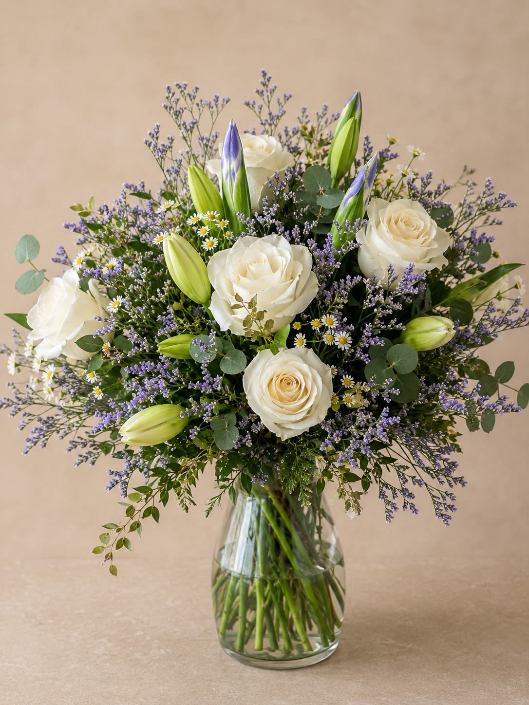 Whispers At Night - Description &amp; Substitution Policy  Elegant, serene, and timeless, Lavender Whisper is designed to bring a sense of peace and beauty to any occasion. This lush garden-inspired arrangement features elegant white roses, fragrant lily buds, delicate lavender statice, charming chamomile daisies, silver dollar eucalyptus, and premium seasonal greenery, all thoughtfully arranged in a classic clear glass vase. Its soft white and lavender color palette makes it a beautiful choice for birthdays, anniversaries, sympathy, get well wishes, thank-you gifts, new baby celebrations, or simply letting someone know you’re thinking of them.  Each arrangement is handcrafted by the designers at House of Bloom using the freshest premium flowers available. Due to seasonal and regional availability, flower varieties, colors, or the vase may be substituted with blooms or containers of equal or greater value while maintaining the overall style, color palette, size, and premium quality of the arrangement. Every design is created with care to ensure it arrives just as beautiful as the one pictured.