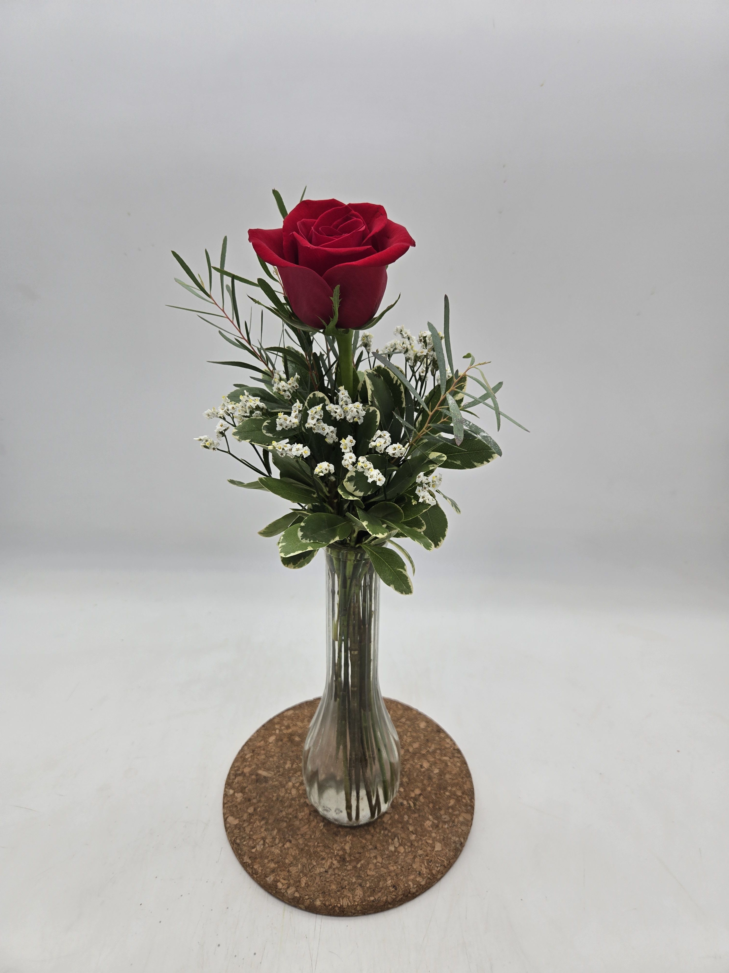 Single red rose in a clear glass vase with small white filler flowers