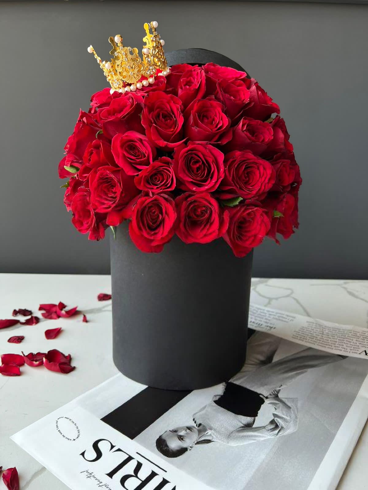 Red roses arranged in a black hat box with a gold crown topper