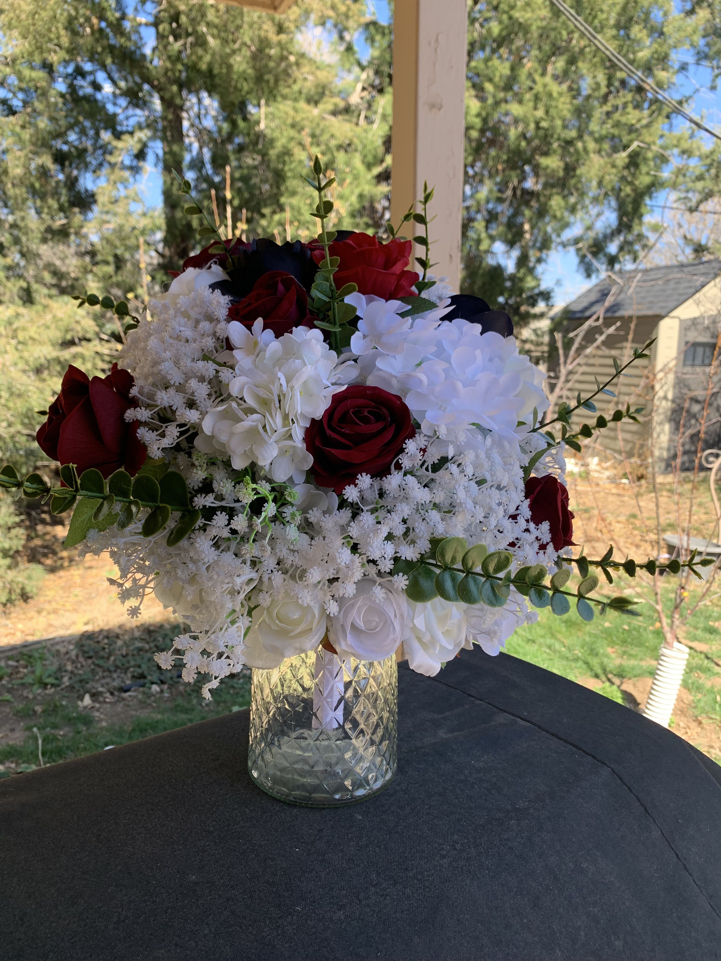Baby Breath Delight - Deep red roses set against clouds of white hydrangea and delicate baby's breath create a timeless wedding bouquet that reads formal, romantic, and unmistakably elegant - perfect as bridal centerpieces or as flowers for weddings at a classic ceremony. The striking red-and-white contrast gives the person you're celebrating a look that feels both dramatic and refined, while long eucalyptus sprigs introduce a soft, green frame that keeps the arrangement feeling fresh and natural.  This full, rounded design mixes deep red and white roses with clustered white hydrangeas and fine white filler flowers for texture, assembled in a textured clear glass vase that shows the stems and gives a polished display presentation. The eucalyptus adds height and airy movement, letting the bouquet breathe on the table or altar; colors present are white, red, green and the dark tones of rose centers that contribute to the overall depth and contrast.  Ideal for brides, anniversary celebrations, or as ceremony centerpieces, this arrangement makes the recipient feel celebrated and seen with classic floral romance. Vase included for easy display; the clear glass finish keeps care simple - fresh water and regular trimming of stems will help preserve the blooms throughout your event.