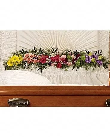 Colorful floral casket spray with roses and daisies on a white casket