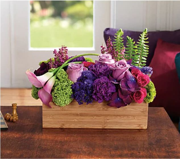 Purple and pink floral arrangement in a wooden box with calla lilies and roses