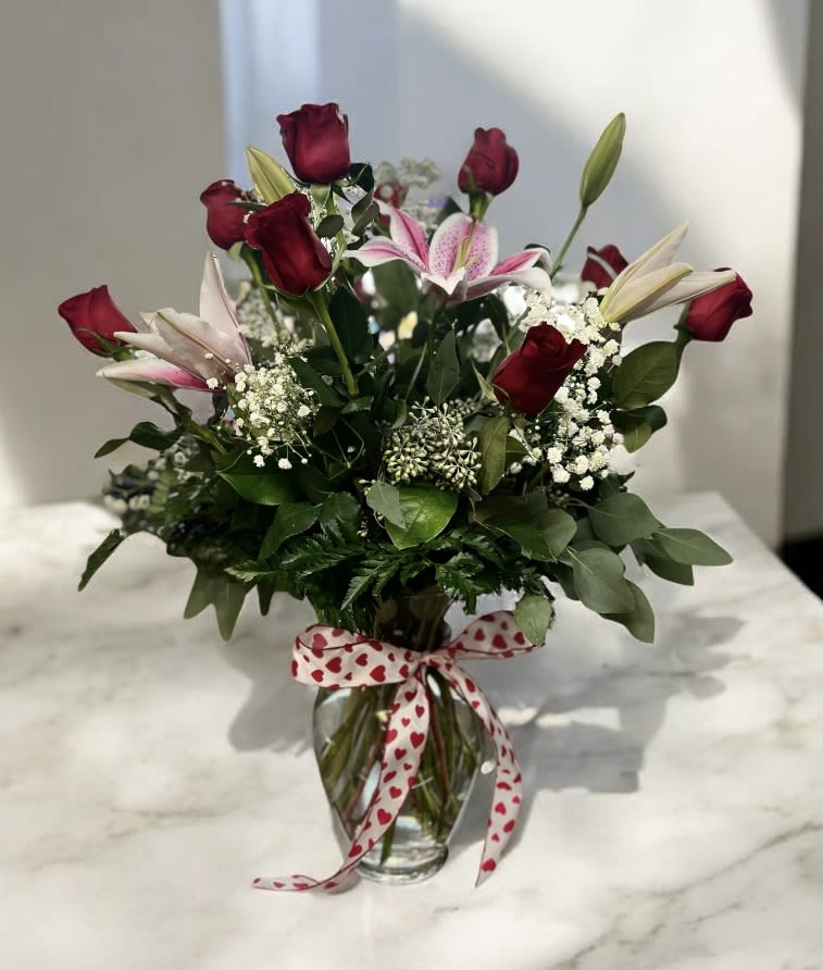 Bouquet of red roses and pink lilies in a glass vase with a heart ribbon