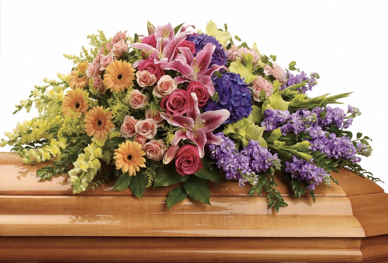 Garden of Sweet Memories Casket Spray - A large, full sympathy spray that reads like a garden of sweet memories-soft pink roses and lilies mingle with warm orange gerbera daisies, lavender snapdragon spikes, and rich purple hydrangea to create a layered, abundant tribute. The arrangement's broad, formal spread balances romantic textures and strong color contrast so the person you're remembering will feel honored with both tenderness and presence.  This piece features a dense mix of roses, lilies, gerbera daisies, snapdragons, hydrangeas, and complementary seasonal blooms in pink, purple, yellow, and orange tones arranged for a full, structured silhouette. Generous proportions and thoughtful color placement give depth and movement, while varied flower sizes and soft greenery provide a comforting, natural touch.  Ideal for memorial services and sympathy occasions, this spray offers a meaningful way to express love, respect, and remembrance-bringing warmth to the setting and comfort to those who come to pay their respects. Available in a substantial size to make a strong visual statement; please contact us for delivery and placement details.