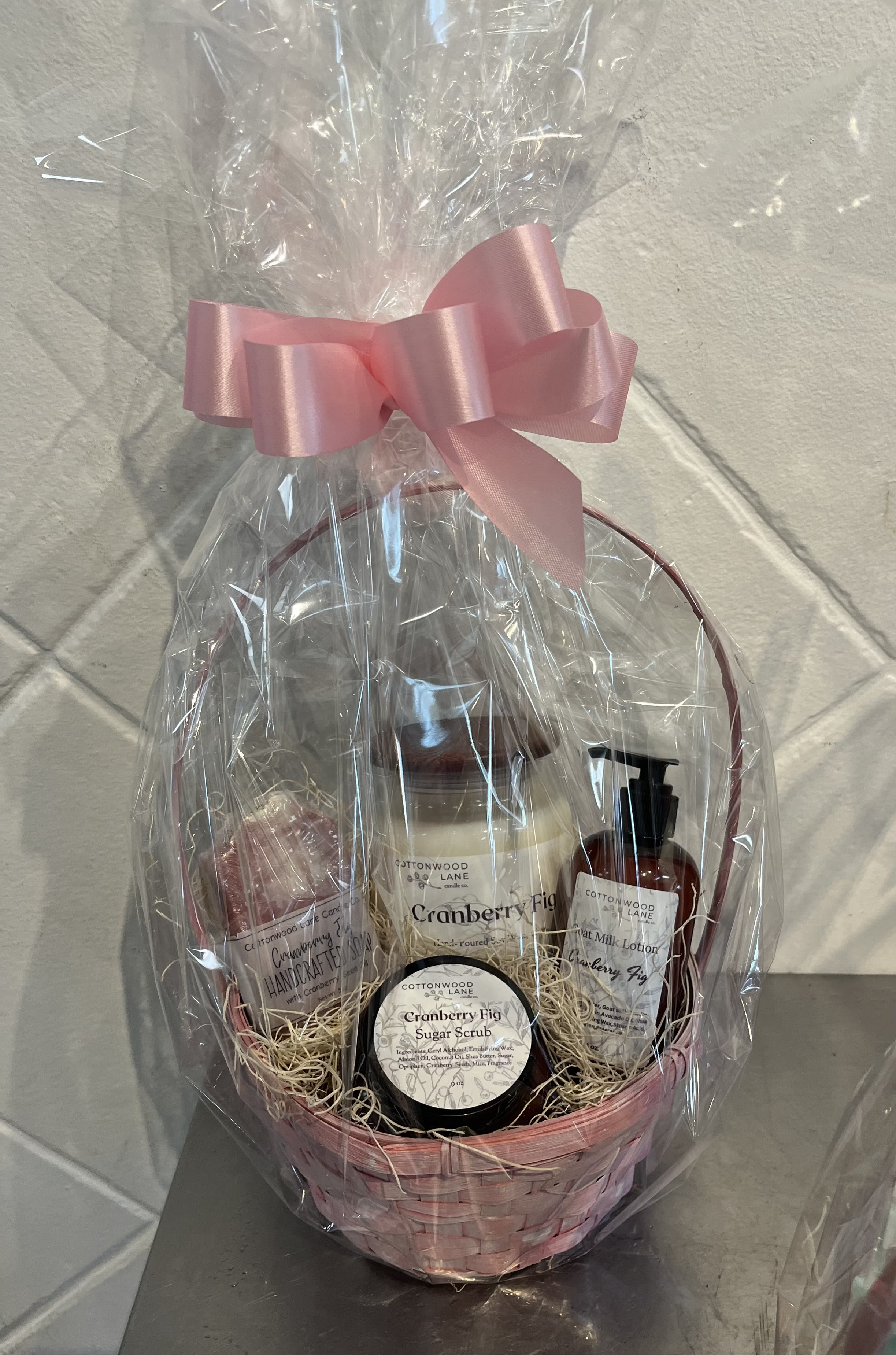 Gift basket with cranberry fig bath products wrapped in clear cellophane and a pink bow