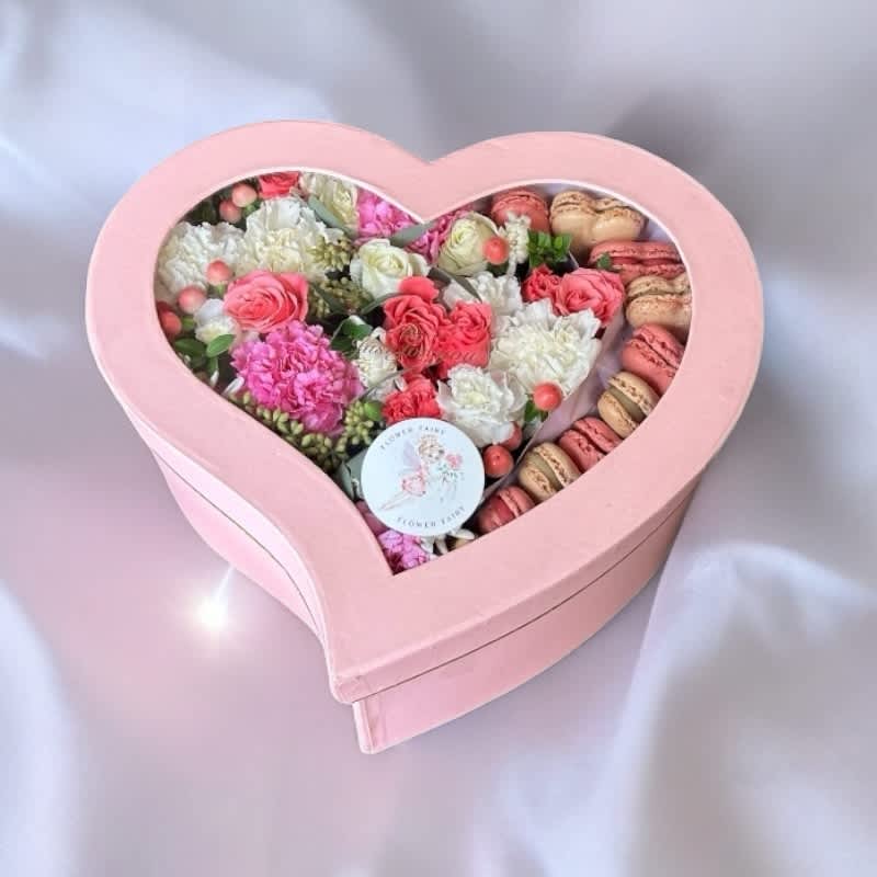 Heart-shaped pink box filled with pink and white flowers and macarons