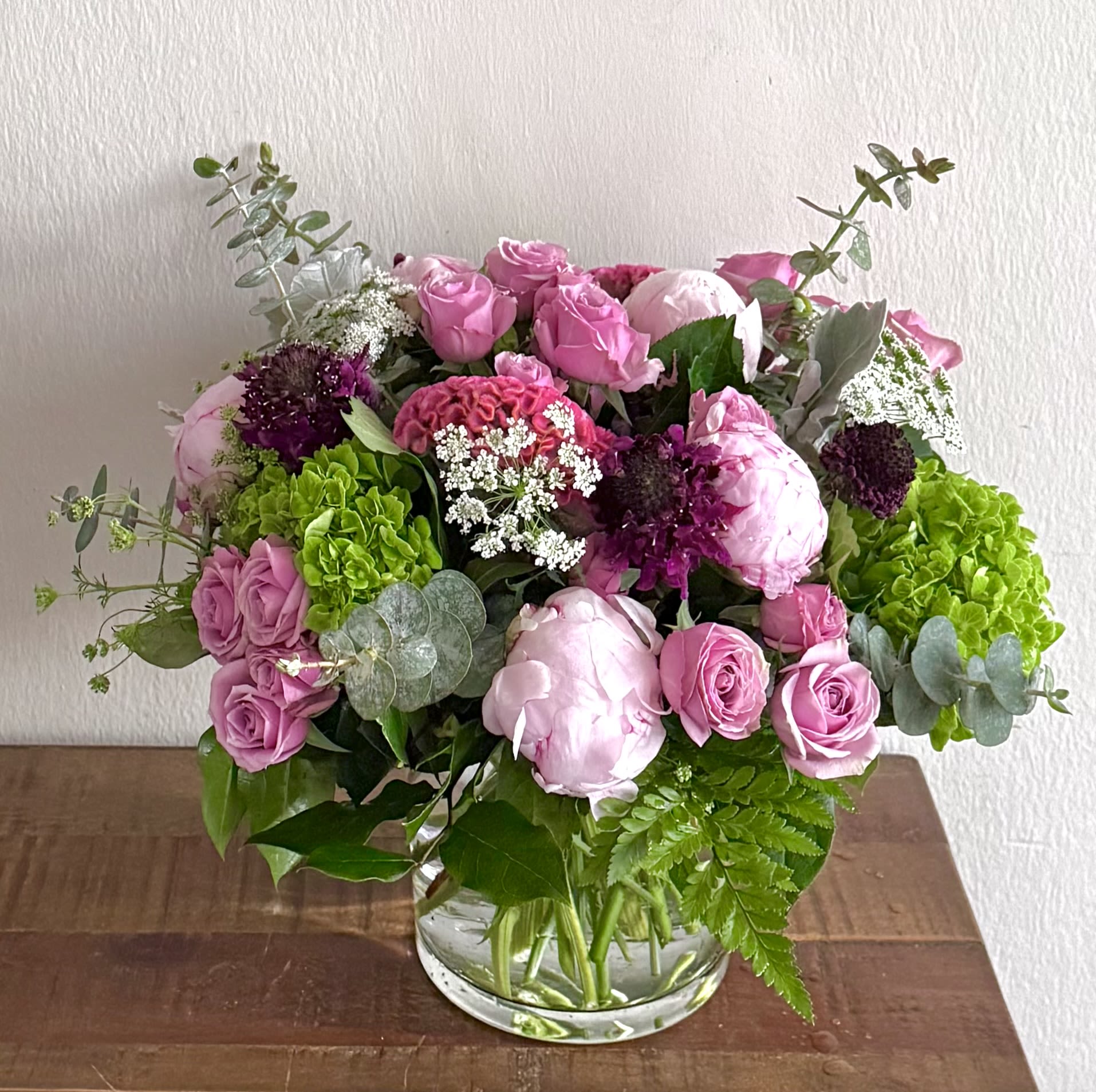 Blushing Garden Elegance - Garden-Style Peony &amp; Rose Arrangement | Washington, DC Flower Delivery  Celebrate life’s most meaningful moments with Blushing Garden Elegance, a lush, garden-inspired floral arrangement designed with premium seasonal blooms in soft blush, lavender, and vibrant green tones. This artistic design features fragrant pink peonies, lavender roses, green hydrangeas, burgundy scabiosa, Queen Anne’s lace, eucalyptus, and seasonal textured flowers arranged in a modern clear glass vase.  Designed with an airy, organic garden style, this bouquet is perfect for birthdays, anniversaries, congratulations, thank you gifts, new baby celebrations, housewarmings, or simply brightening someone’s day. Each arrangement is handcrafted by Shoots and Blooms of DC using the freshest seasonal flowers, so every design is one-of-a-kind while maintaining its elegant garden aesthetic. Garden-style arrangements with organic movement and seasonal blooms are a sought-after floral design style.  
