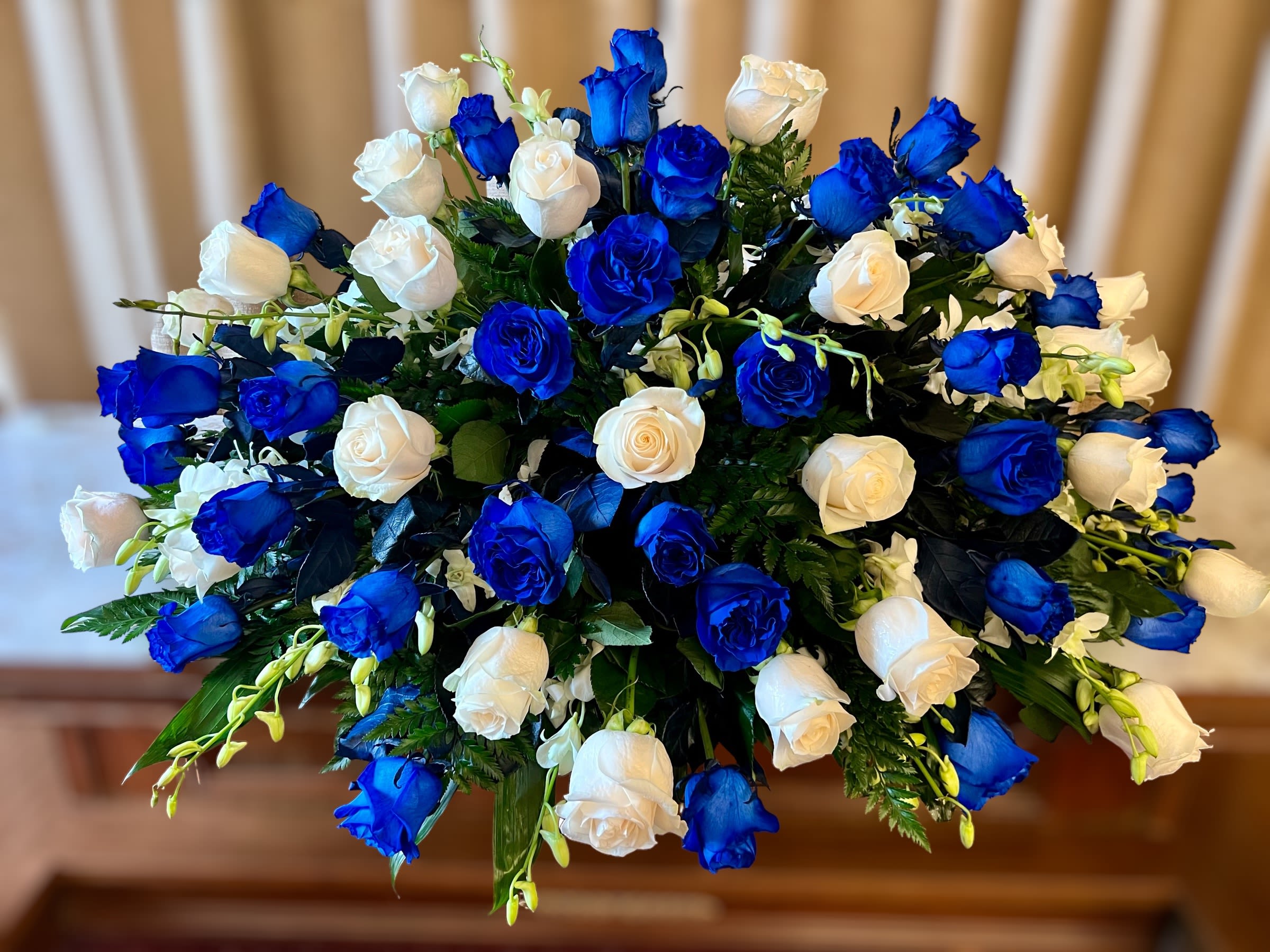 Oval arrangement of blue and white roses with accent flowers in a dense spray.