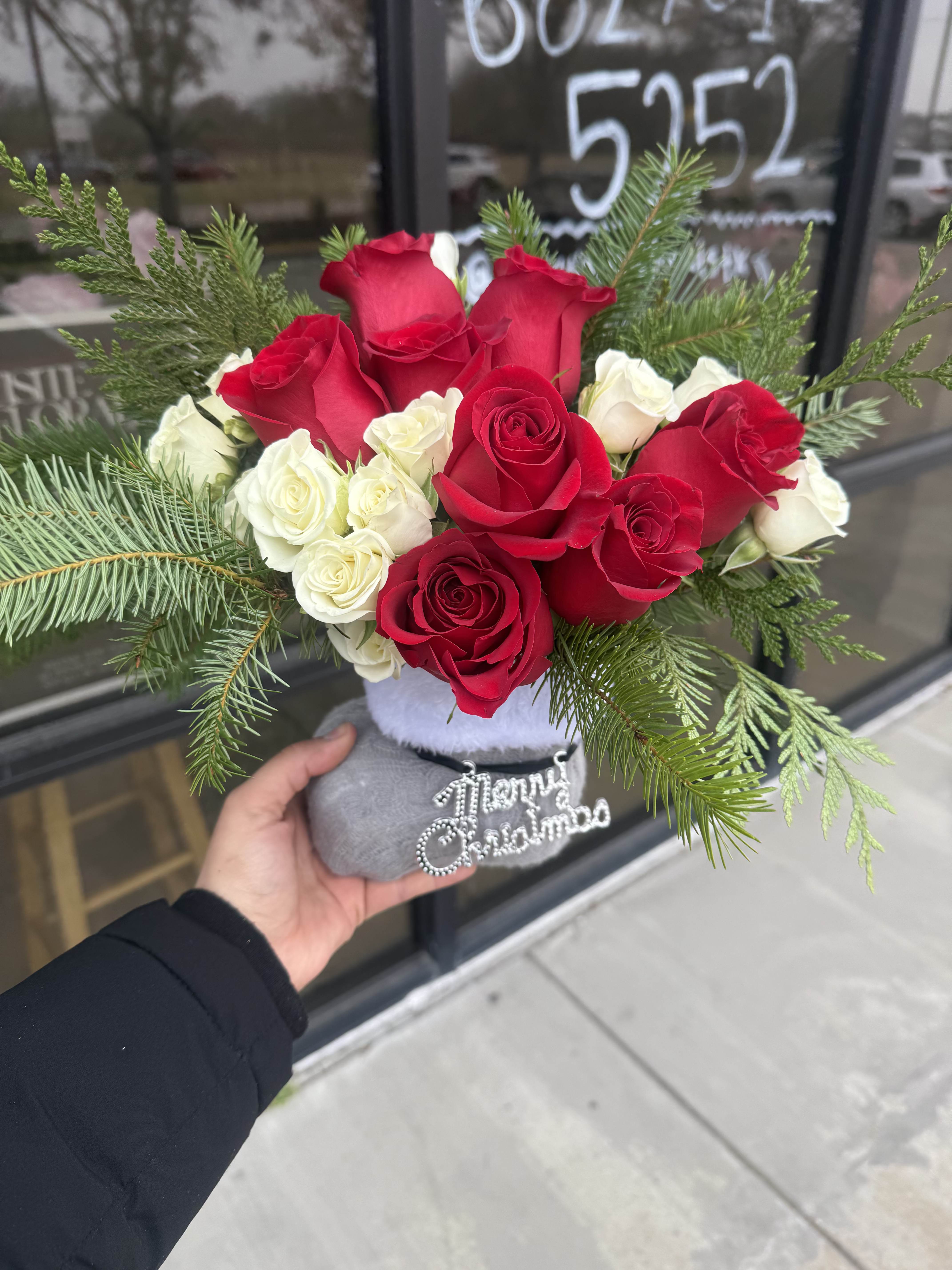 Red and white roses arranged with evergreen branches in a small holiday container.