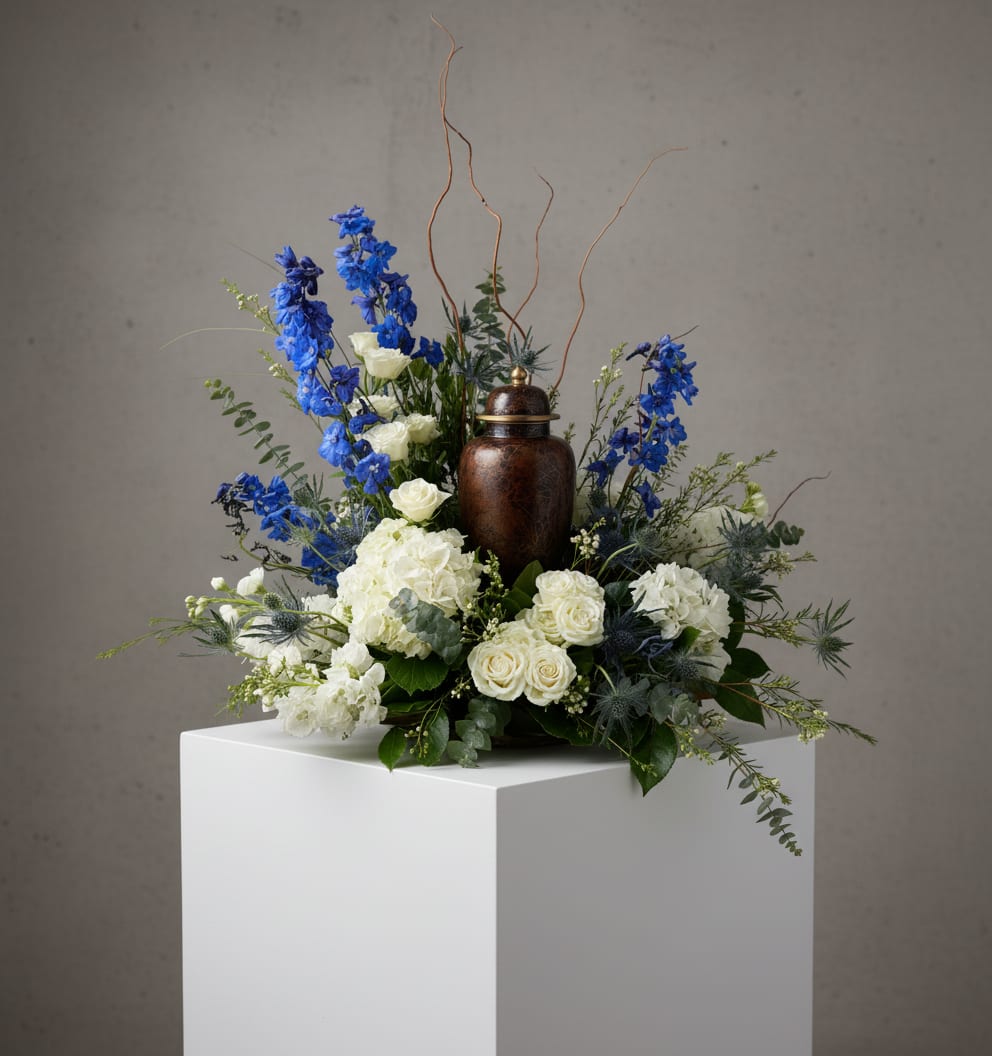 Reflections - A graceful tribute designed to honor a life beautifully lived, Reflections features a timeless collection of premium blooms artfully arranged. Soft white roses, hydrangea, and seasonal accent flowers are complemented by airy blue delphinium, textured botanicals, and flowing greenery, creating a design that is both elegant and comforting. Thoughtfully crafted with natural movement and refined detail, Reflections offers a meaningful expression of love, remembrance, and enduring peace during life's most difficult moments.