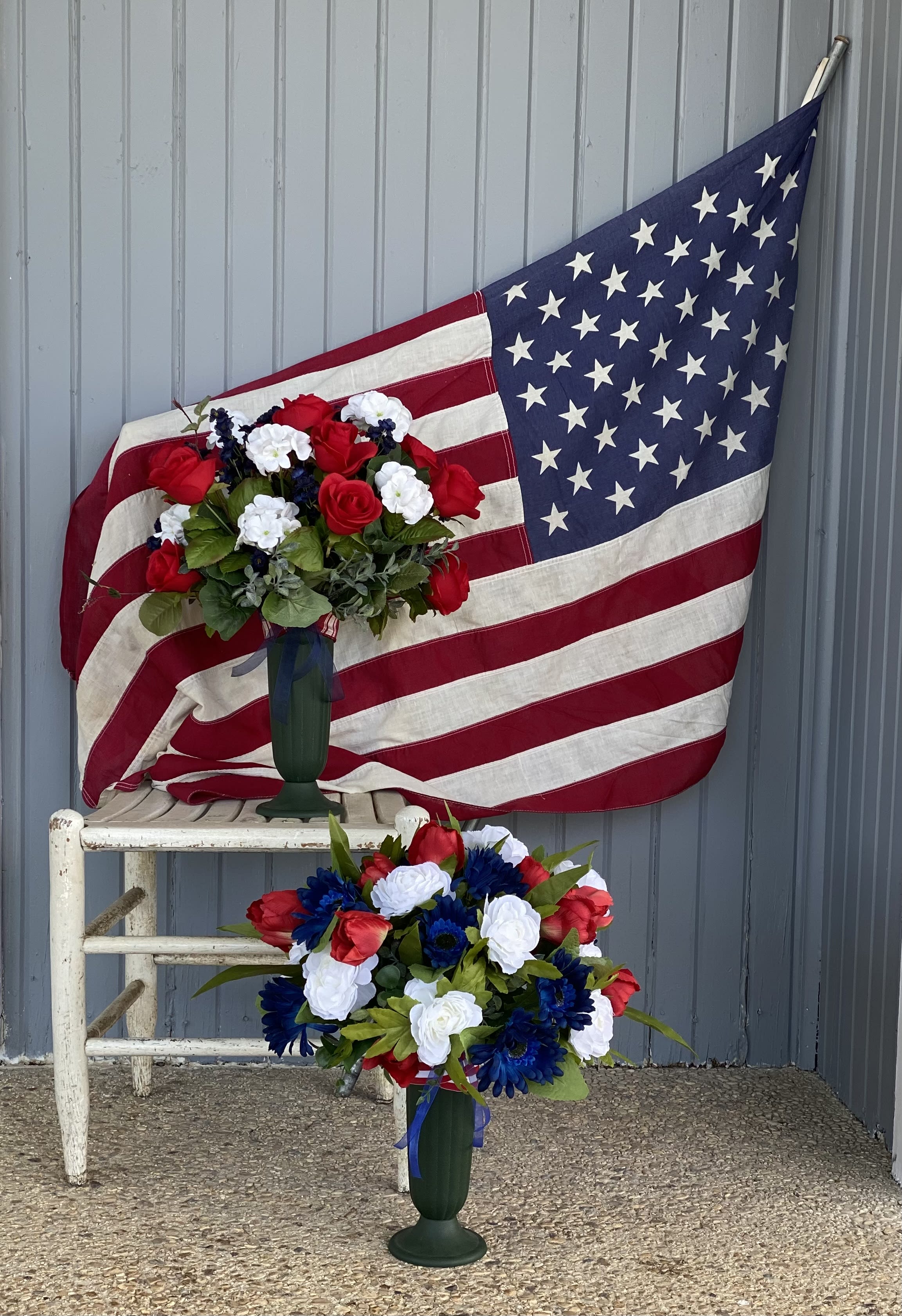 Two red, white, and blue floral arrangements in green vases before an American flag.