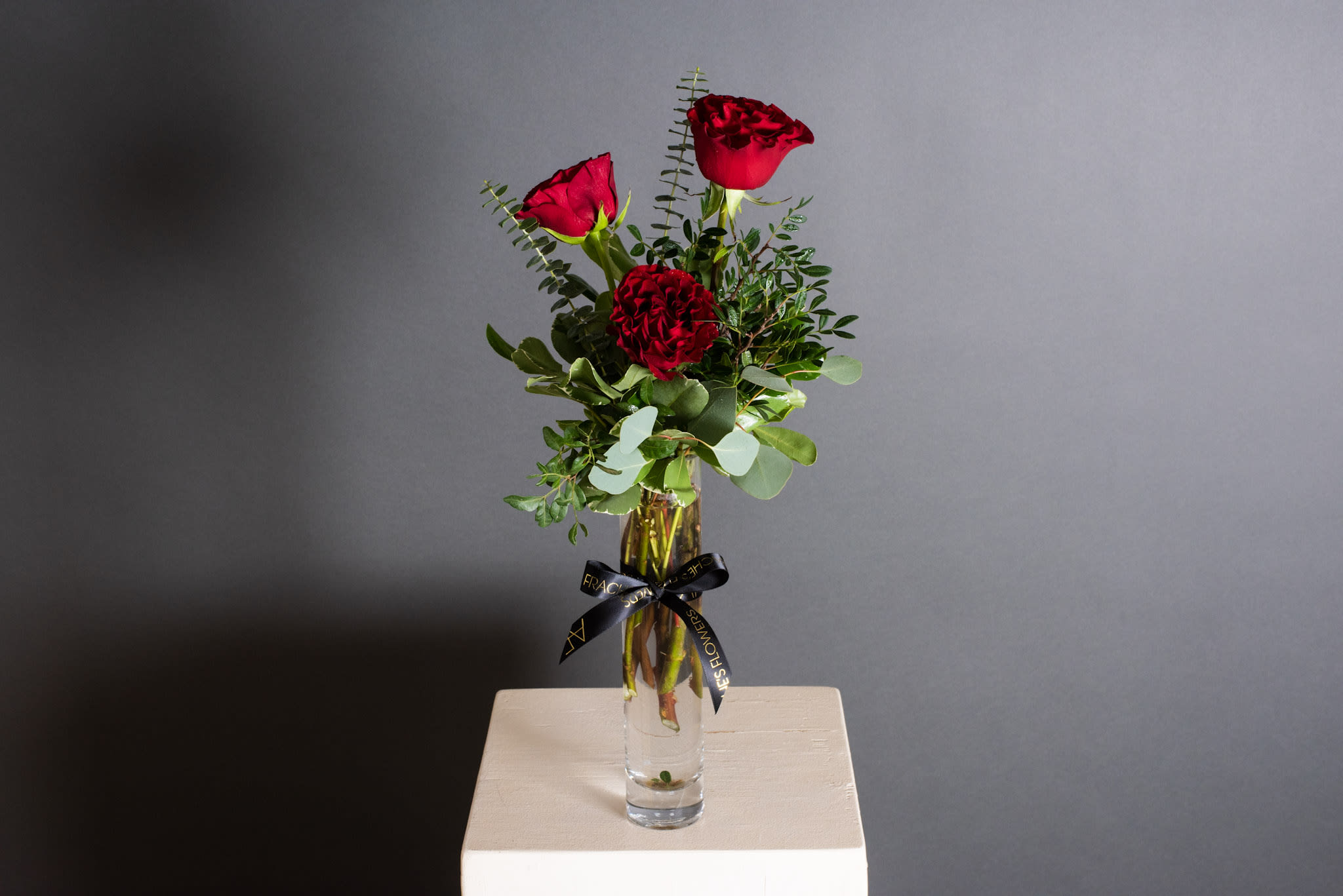 Red roses arranged in a clear glass vase with greenery