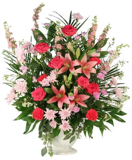 Timeless Inspiration Funeral Flowers - Strong and radiant, reflecting the vibrant life that has passed. Timeless Inspiration is an elegant display of sympathy. Bursting with pink roses, carnations, lilies, cushion poms, and more, this arrangement celebrates a vibrant spirit and a heart full of love. It stands as a loving tribute, honoring cherished memories and the everlasting impact they leave behind.  Includes: Hot Pink Carnations, Purple Mini Carnations, Pink Larkspur, Pink Lilies, Pink Cushion Poms, Hot Pink Roses, Waxflower, Greens: Seeded Eucalyptus, Cocculus, Salal Tips, Tepe Palm, White Urn.