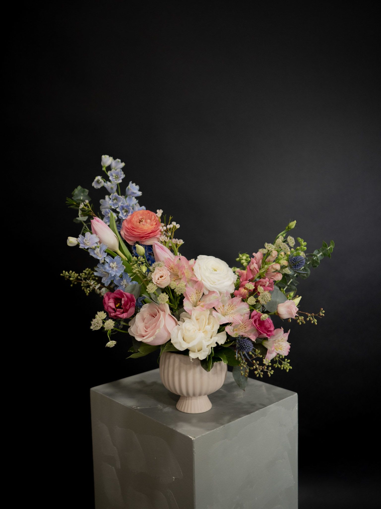 Mixed pink, white, and blue flowers in a ribbed pedestal vase