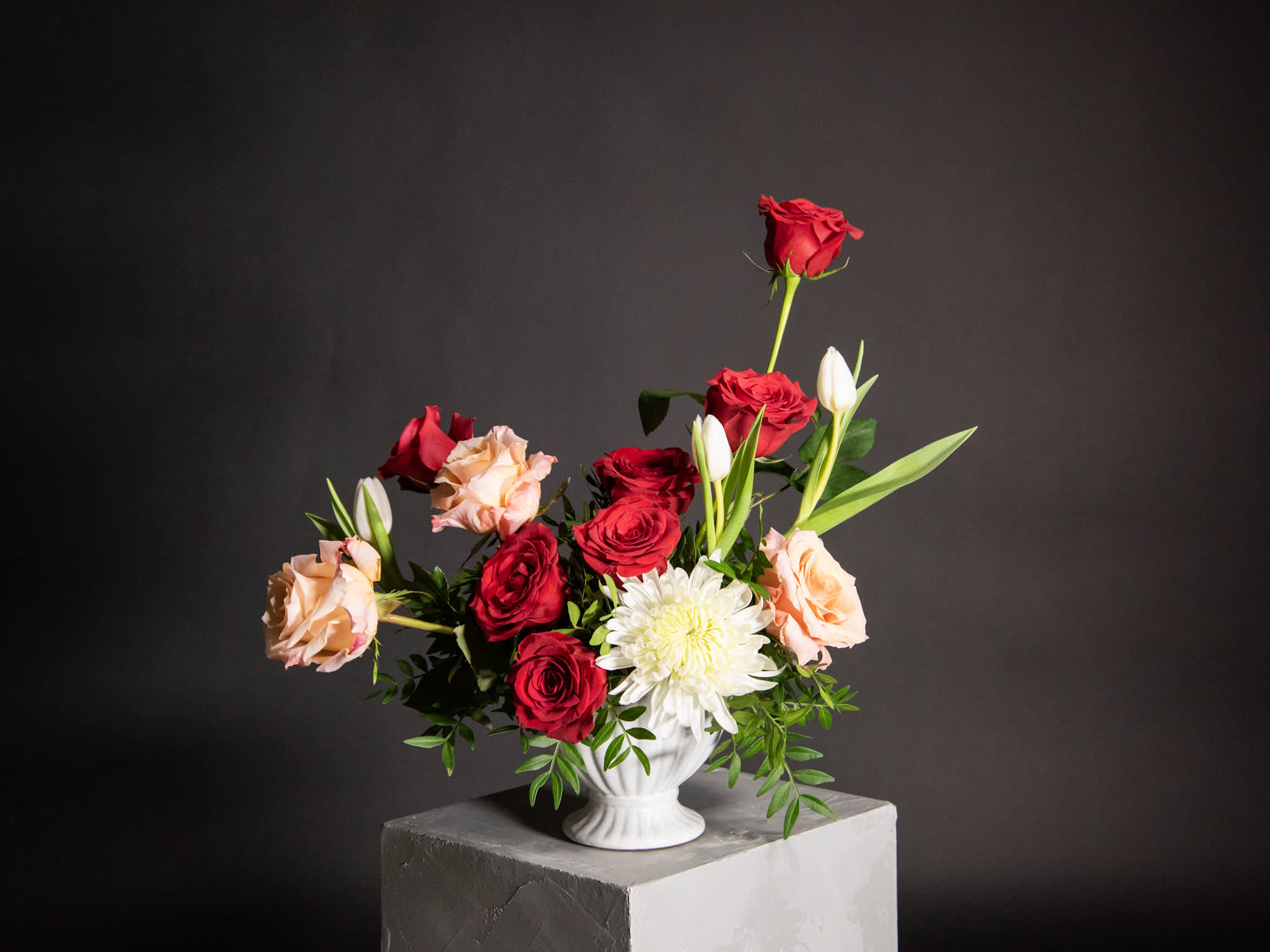 Red and peach roses arranged with white blooms in a white vase