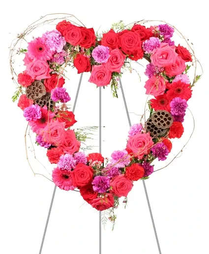Heartfelt Array Standing Wreath - Embracing genuine emotion, Heartfelt Array displays vibrancy with its hot pink and red roses and gerberas, and purple moon carnations, accented by dried grapevine and lotus pods. Each bloom tells a story of passion and remembrance. This spray is a heartfelt gesture to comfort and console during times of loss.  Includes: Open Heart Mache, Seeded Eucalyptus, Myrtle, Plumosus, Red Carnations, Purple Moon Carnations, Hot Pink Gerberas, Hot Pink Roses, Purple Waxflower, Red Roses, Red Gerberas, Dried Lotus Pods, Grapevine.