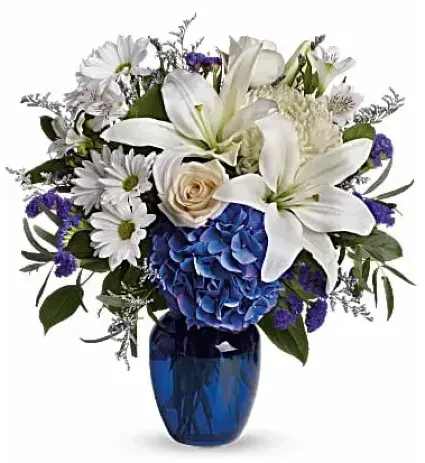 Beautiful In Blue Flower Arrangement - Blooms such as blue hydrangea, crème roses, graceful white oriental lilies, white alstroemeria, a white disbud mum, purple statice and lavender limonium are accented by seeded eucalyptus and salal in a stunning cobalt blue glass vase.