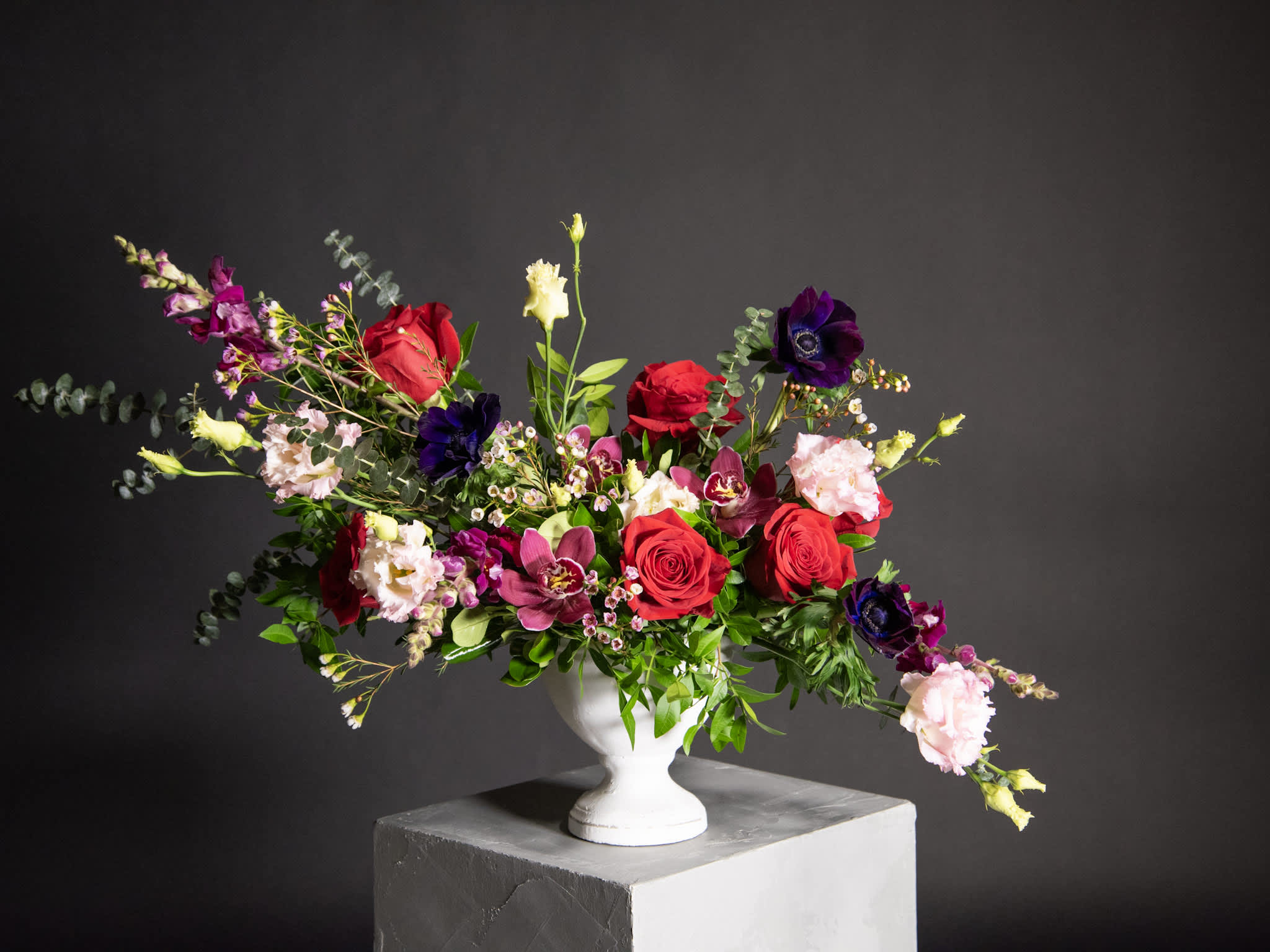 Mixed bouquet of red roses, purple blooms, and pale pink flowers in a white vase