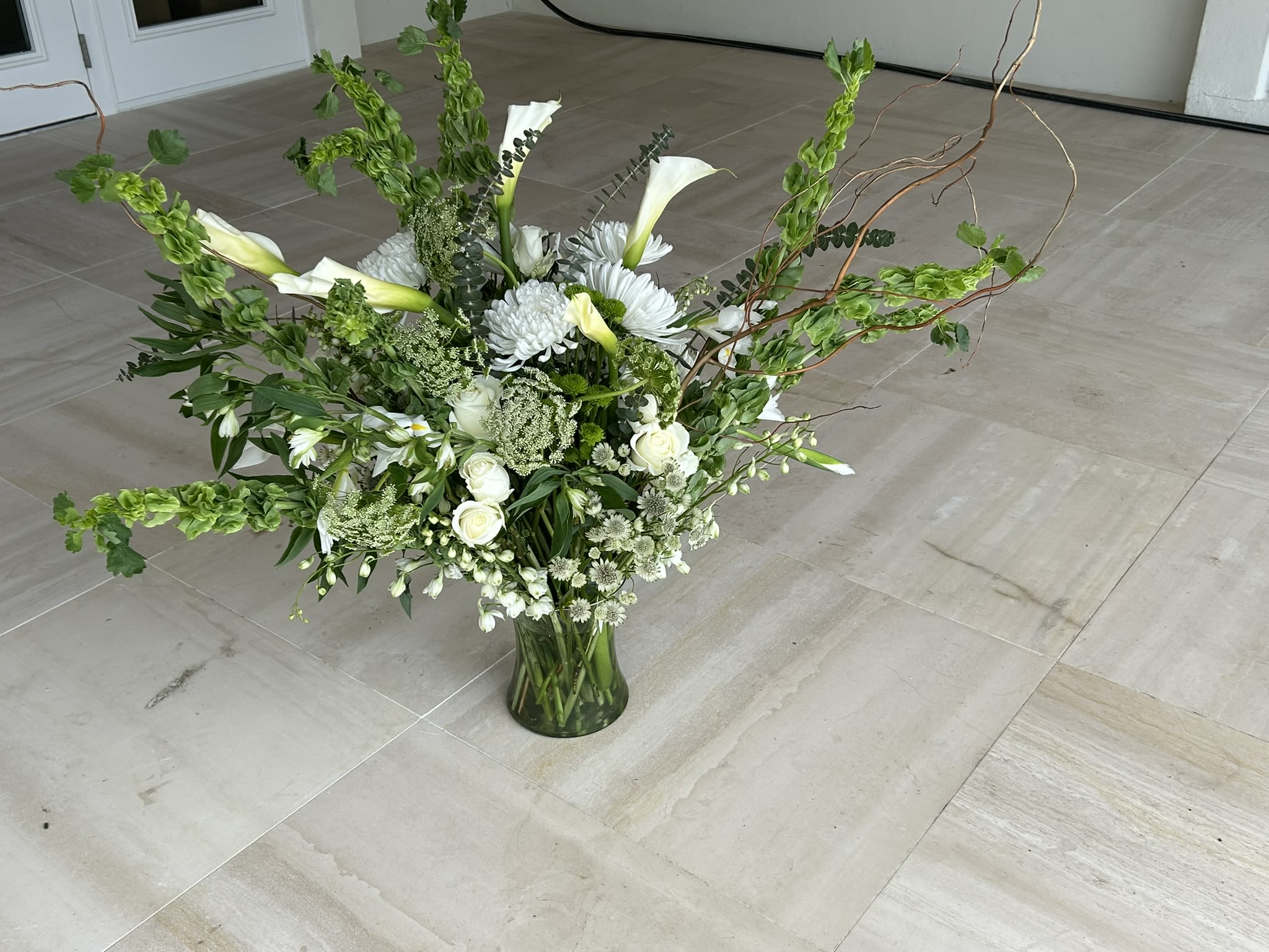 Spring bells - You cant miss this prominent display of Irish bells, Roses, Large Calli Lillis, along with mix of unusual accompanying seasonal white flowers and Curly Willi Branch. Far more impressive in person over 2.5 feet wide