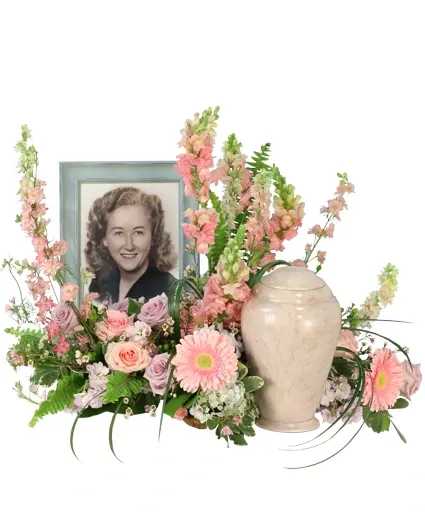 Delicate Remembrance Cremation Flowers - This heartfelt memorial arrangement is adorned with pink, lavender, and blue hues, embodying the essence of grace and tranquility. In soothing hues, larkspur, roses, snapdragons, stock, hydrangeas, and gerberas intertwine, honoring a life cherished and remembered. Order Delicate Remembrance to honor your loved one today.  Includes: Mache Form, Laid Flat, Green Lily Grass, Variegated Pittosporum, Salal, Feather Fern, Pink Mini Carnations, Pink Gerberas, Blue Hydrangeas, Green Hypericum, Pink Larkspur, Pink Roses, Pink Snapdragons, Lavender Stock, Pink Waxflower, Lavender Roses.