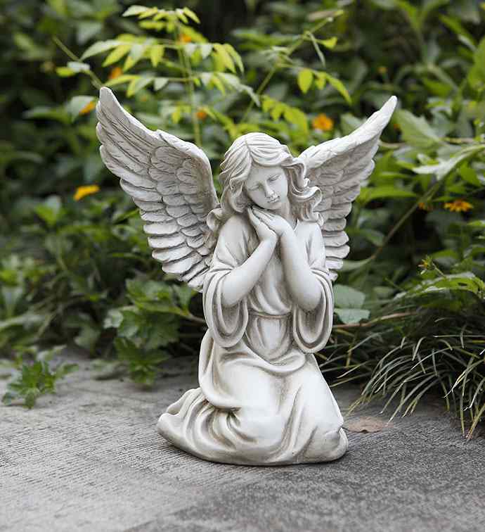 White angel statue kneeling with folded hands in a garden setting