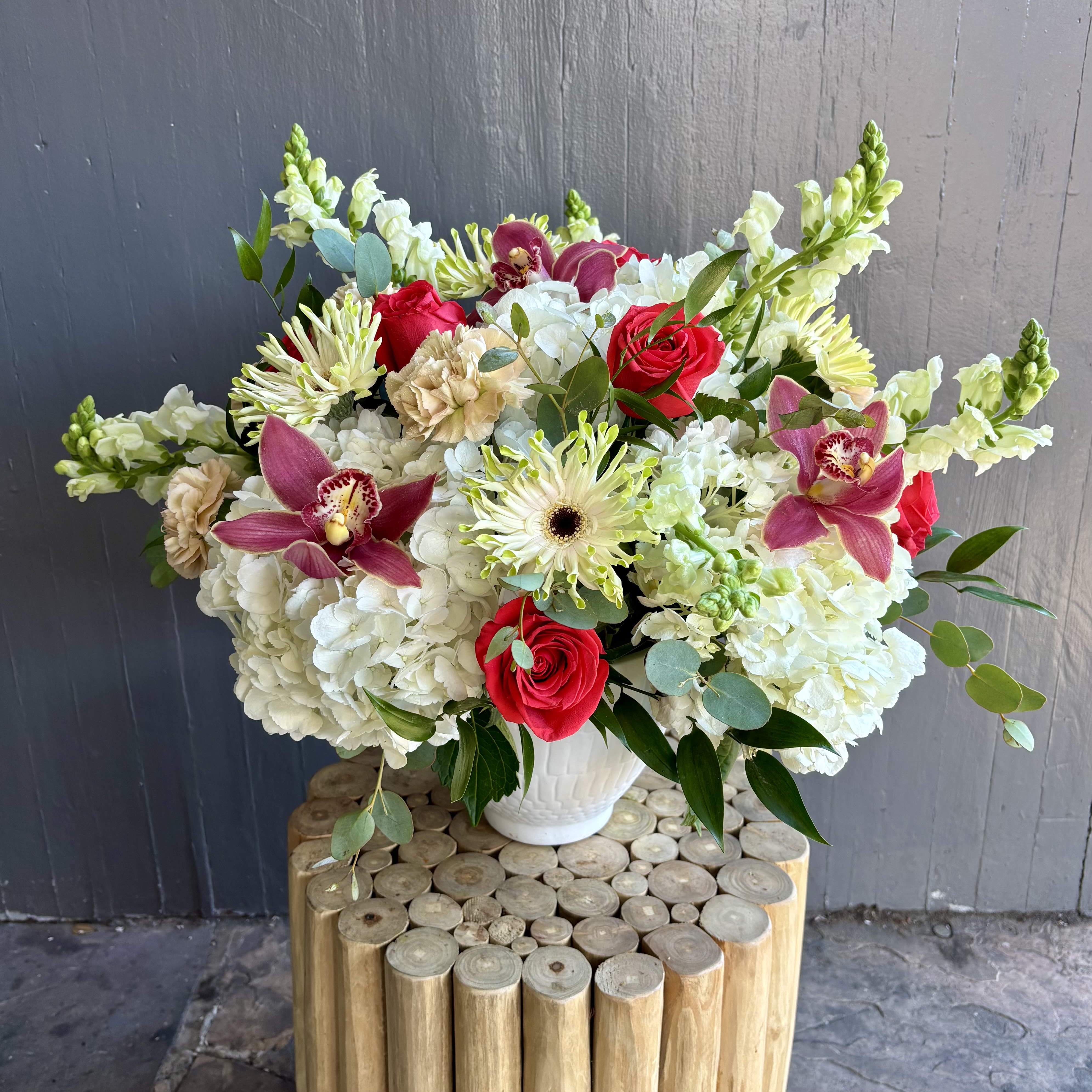 Bouquet of red roses, white hydrangeas, and pink orchids in a white vase