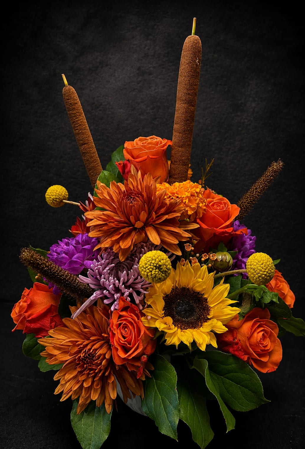 Fall Garden - Bright, bold orange roses and a single sunny sunflower anchor this flower arrangement for a confident autumn statement-perfect as an anniversary bouquet, birthday surprise, or Thanksgiving centerpiece. The upright silhouette and dramatic colors make it a warm "thinking of you" gift that also reads beautifully for get well, thank you, sympathy, or just-because moments.  This dense, layered design features orange and purple chrysanthemums, lavender-toned stock, lush hydrangea texture and mixed seasonal blooms arranged in a classic vase, with two tall brown cattail-like accents rising above the mix for added height and rustic interest. The saturated yellow, green, red and mixed-color palette creates strong contrast and a festive, energetic mood that suits summer through winter celebrations alike.  Give this to someone who should feel noticed-she'll feel genuinely celebrated by the rich colors and bold texture. Available in a compact, lower-profile vase; for best results, change the water every other day and trim stems slightly when arranging to extend freshness.