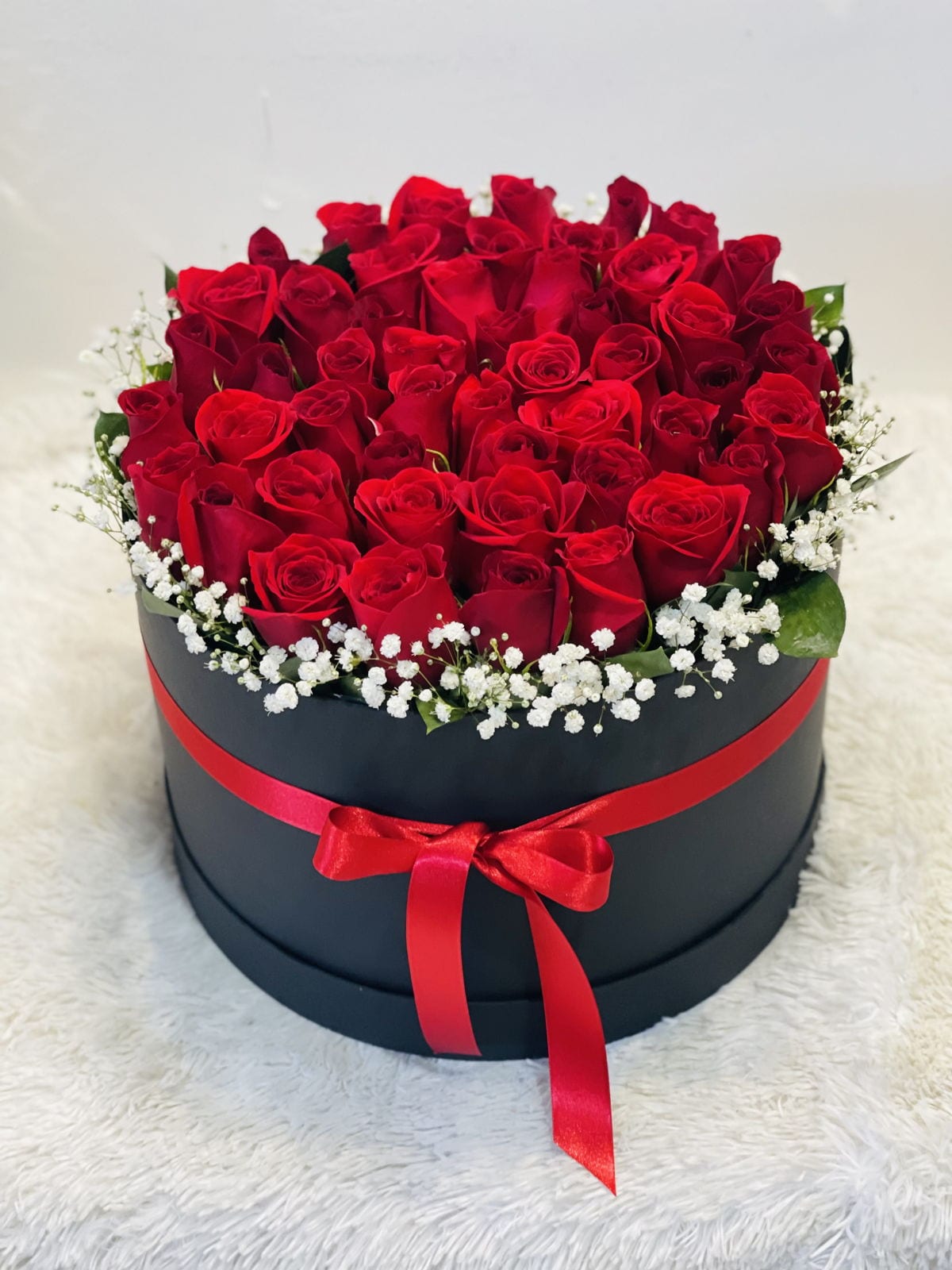 Red roses arranged in a round black box with a red ribbon.