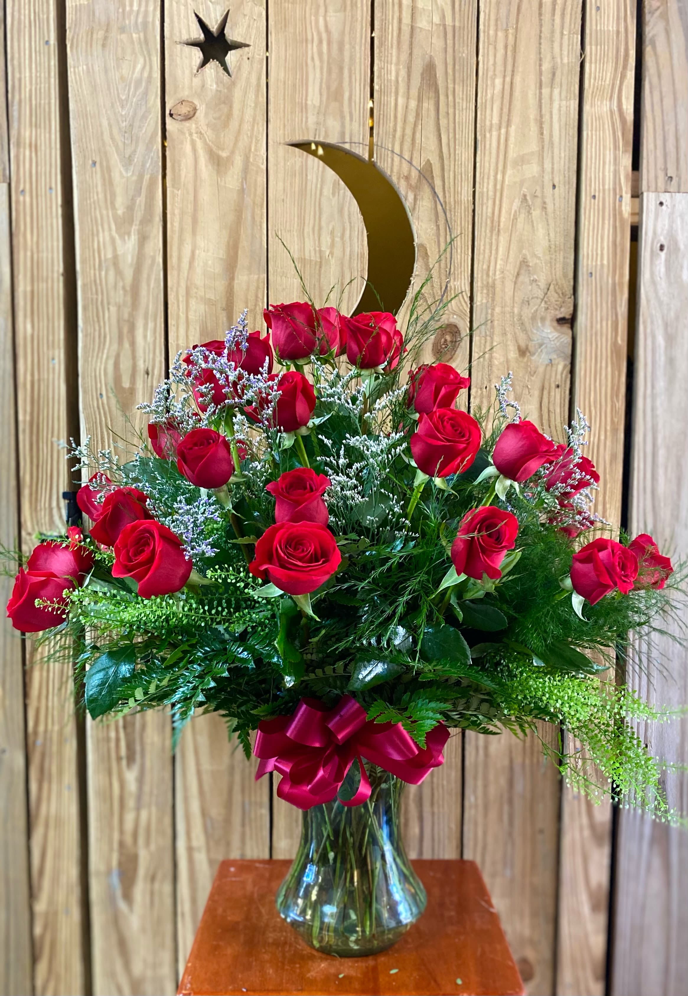 Tall arrangement of red roses with white filler flowers in a clear glass vase with a red bow.